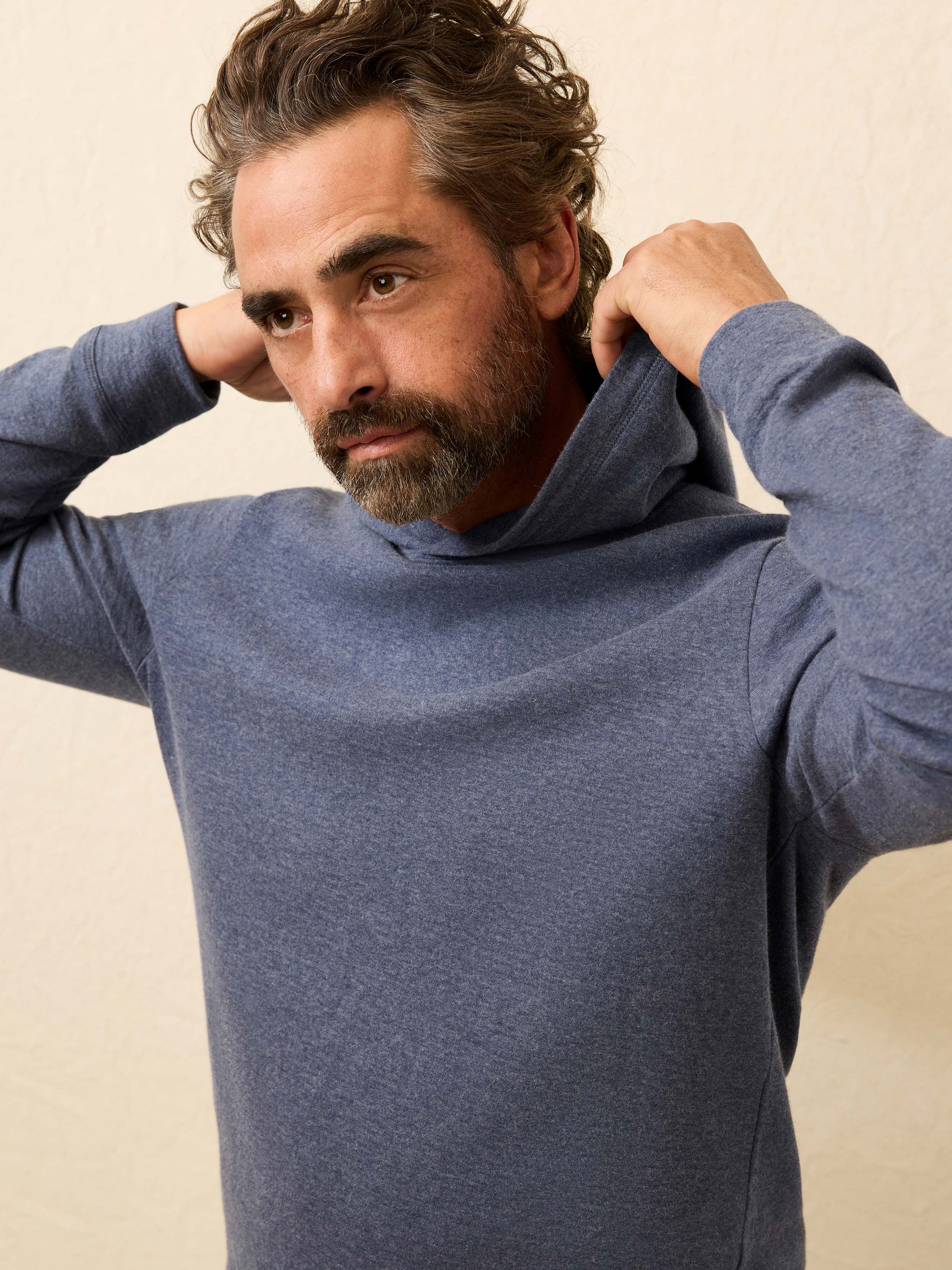 Man wearing a blue cashmere hoodie against a beige background