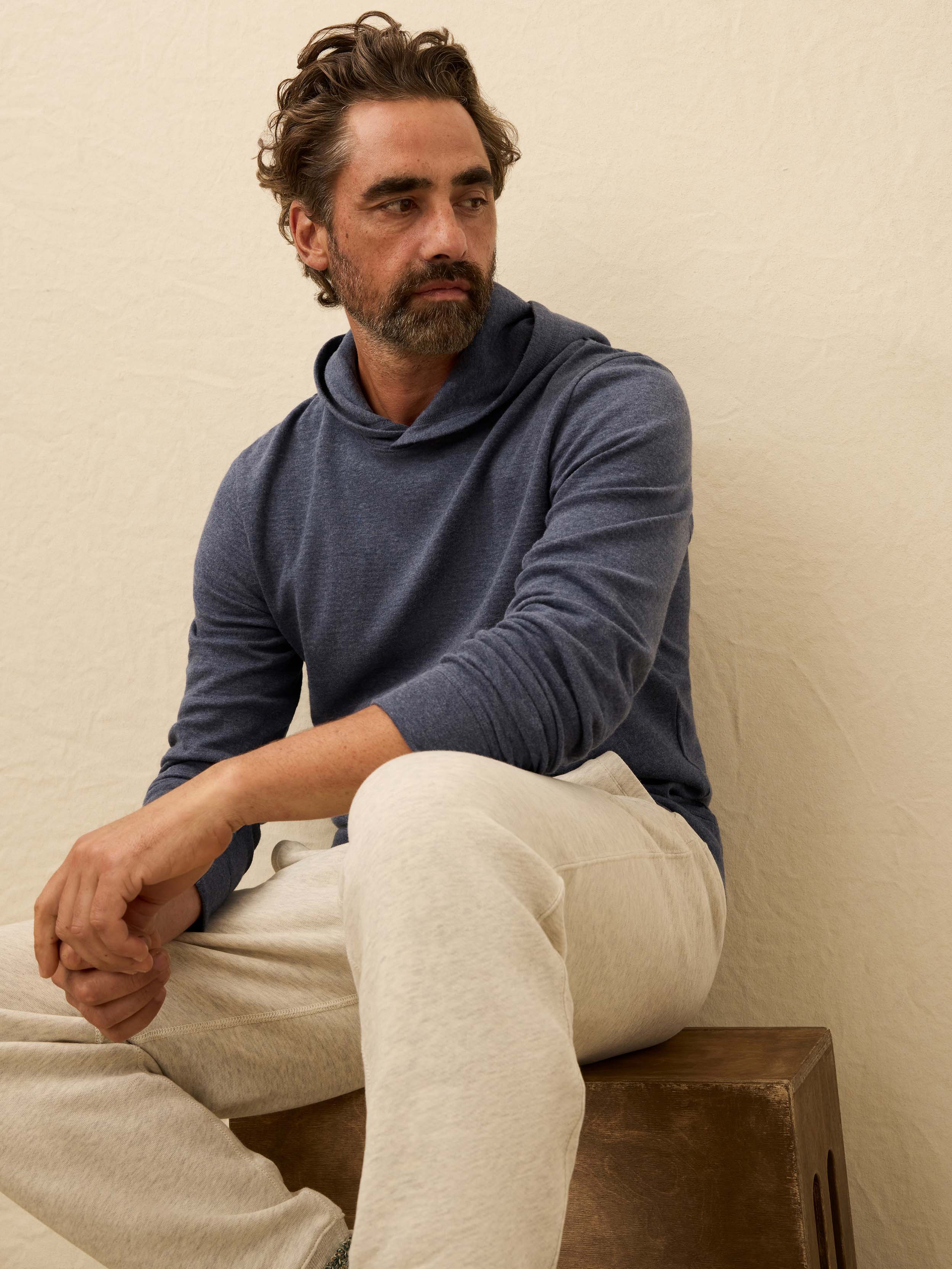 Man wearing a blue cashmere hoodie with sweatpants against a beige background