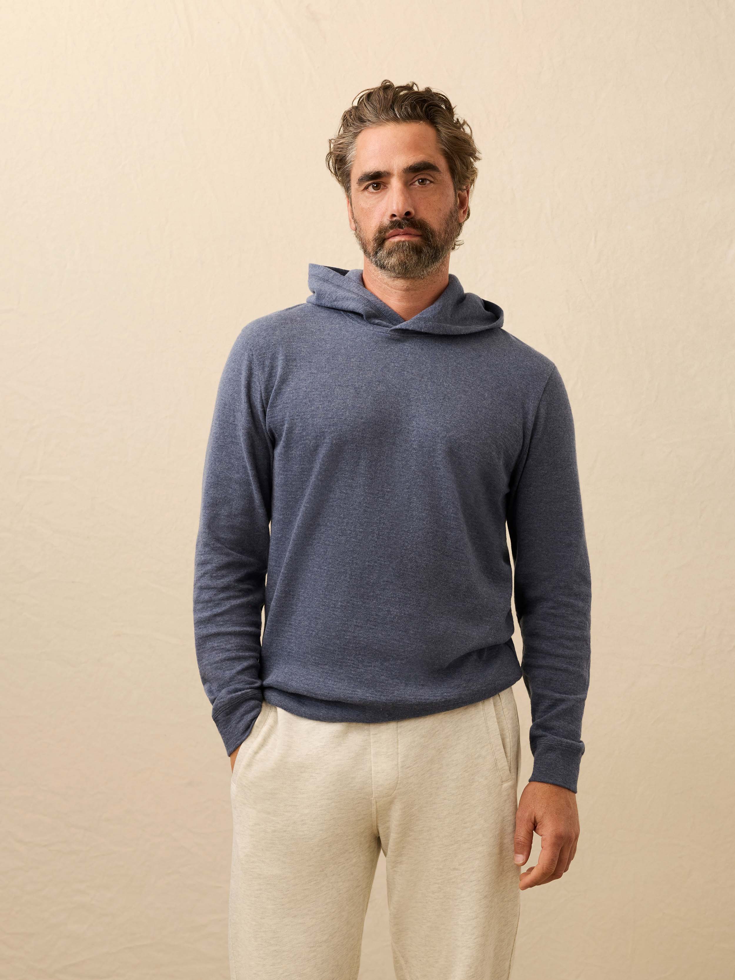Man wearing a cashmere hoodie with sweatpants against a beige background
