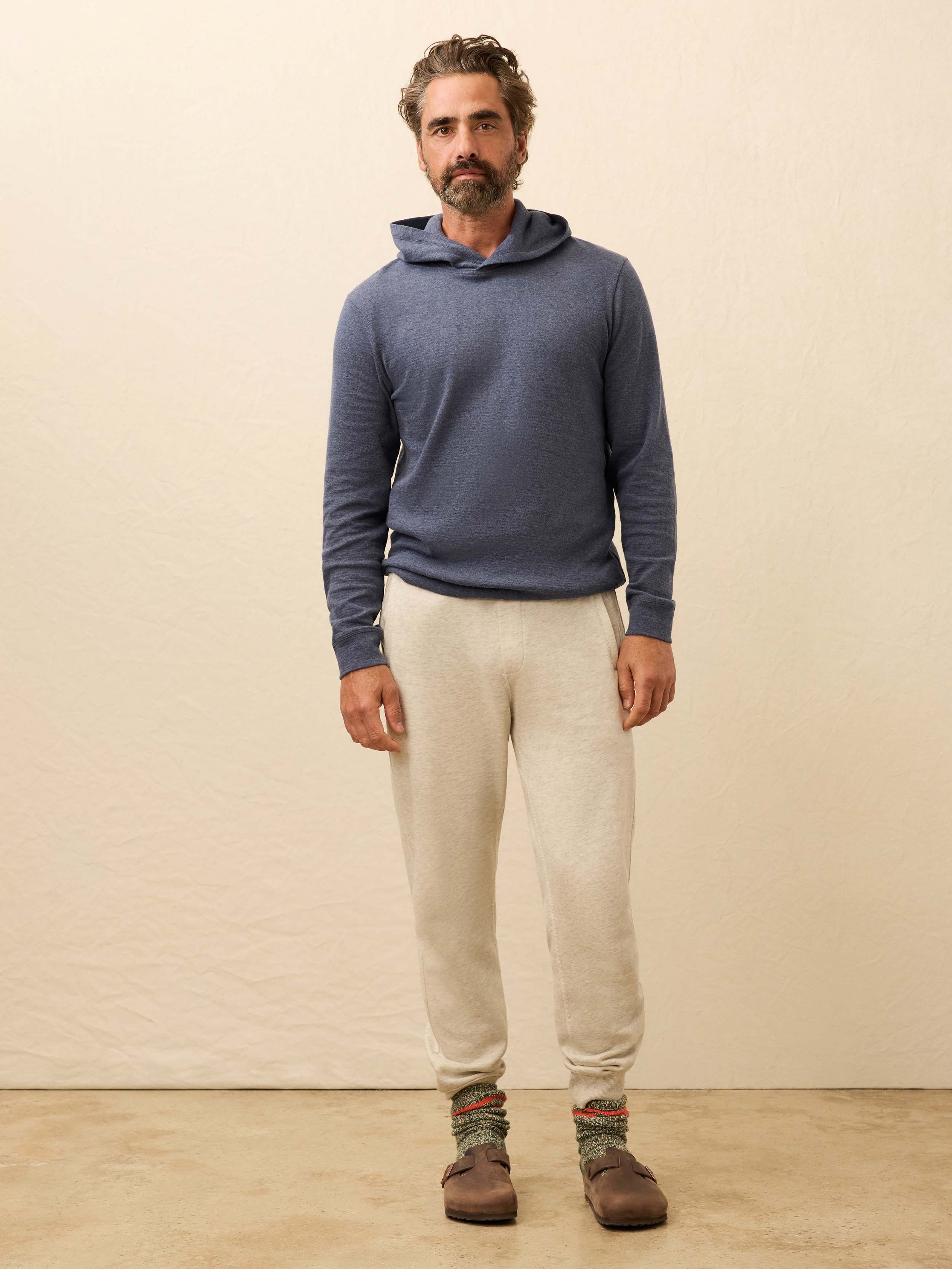 Man wearing a blue cashmere hoodie with sweatpants against a beige background