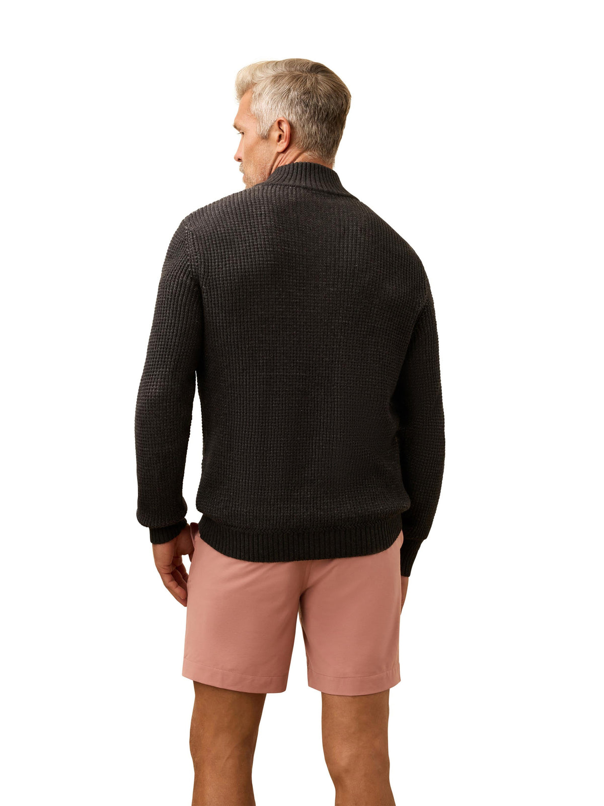 A man viewed from behind wearing a dark grey sweater and salmon colored shorts, image 3 of 3