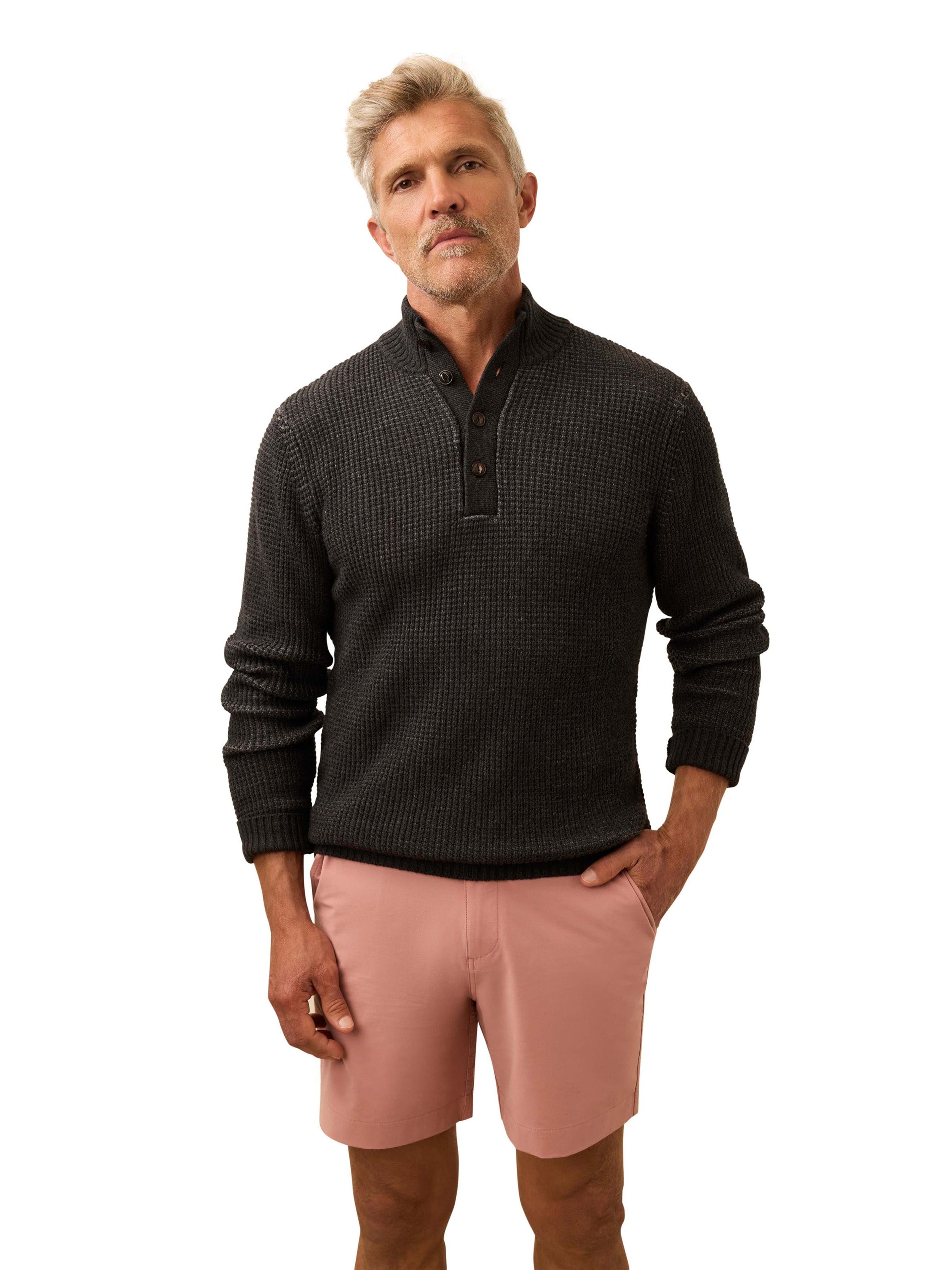 A man wearing a dark grey sweater and salmon colored shorts