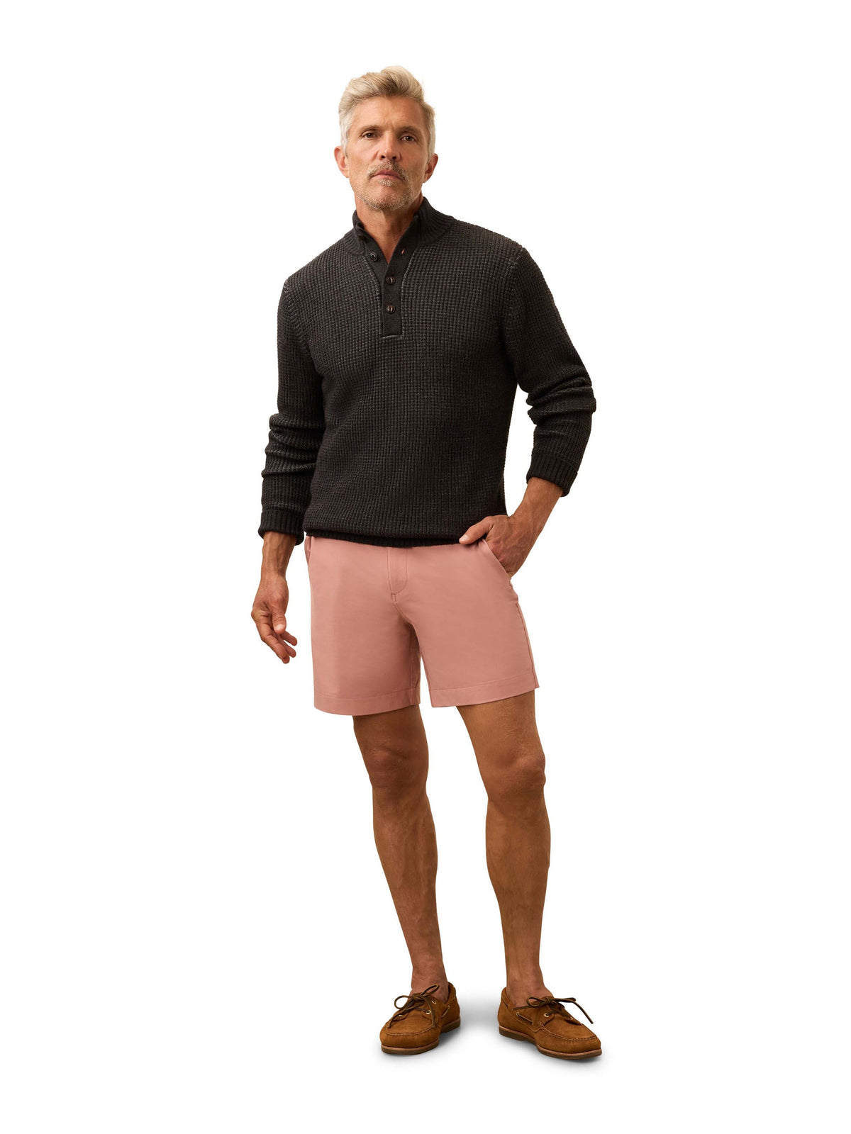 A man wearing a dark grey sweater and salmon colored shorts, image 2 of 3