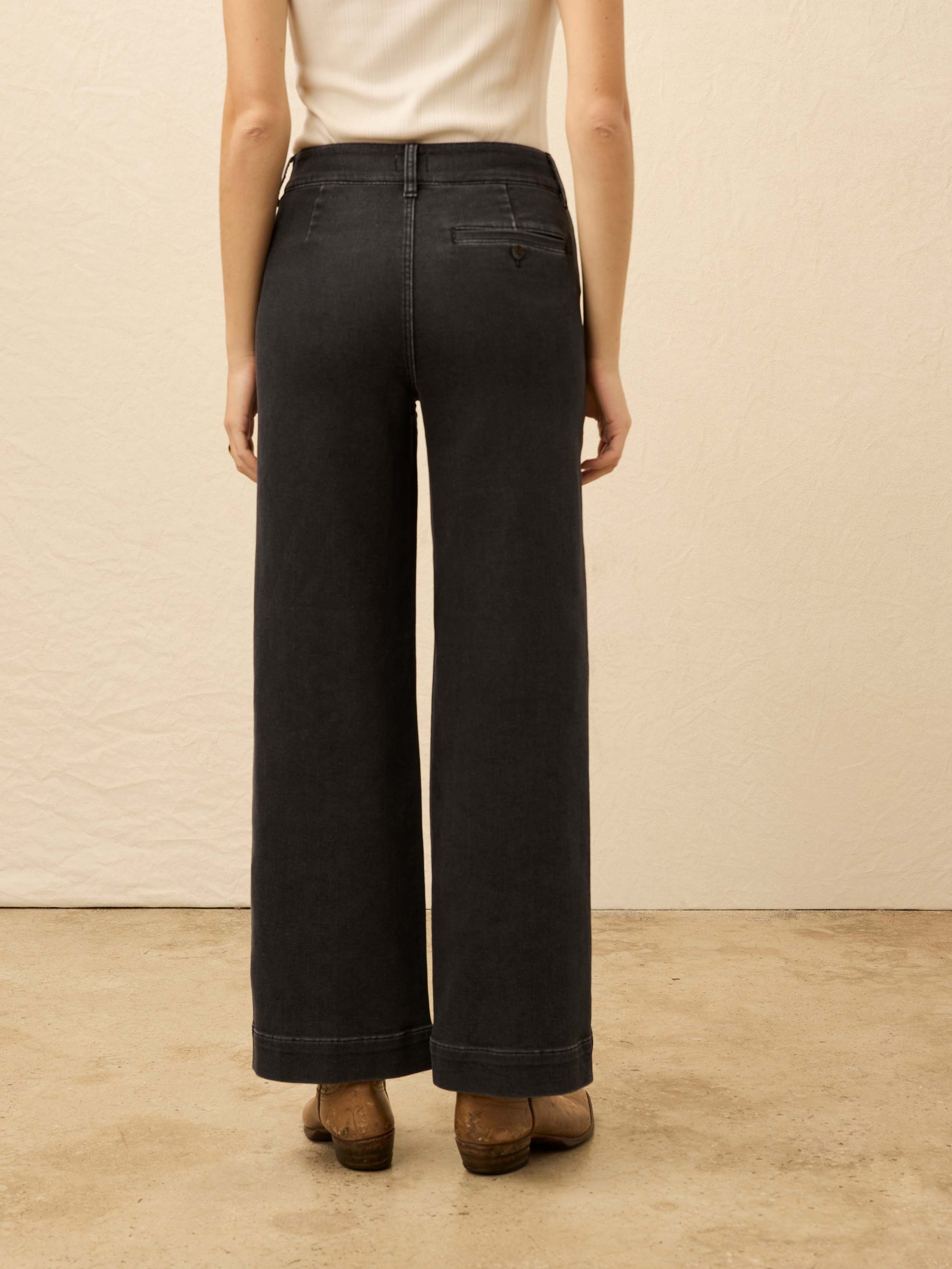 Woman wearing black wide-leg jeans and a white top against a beige background