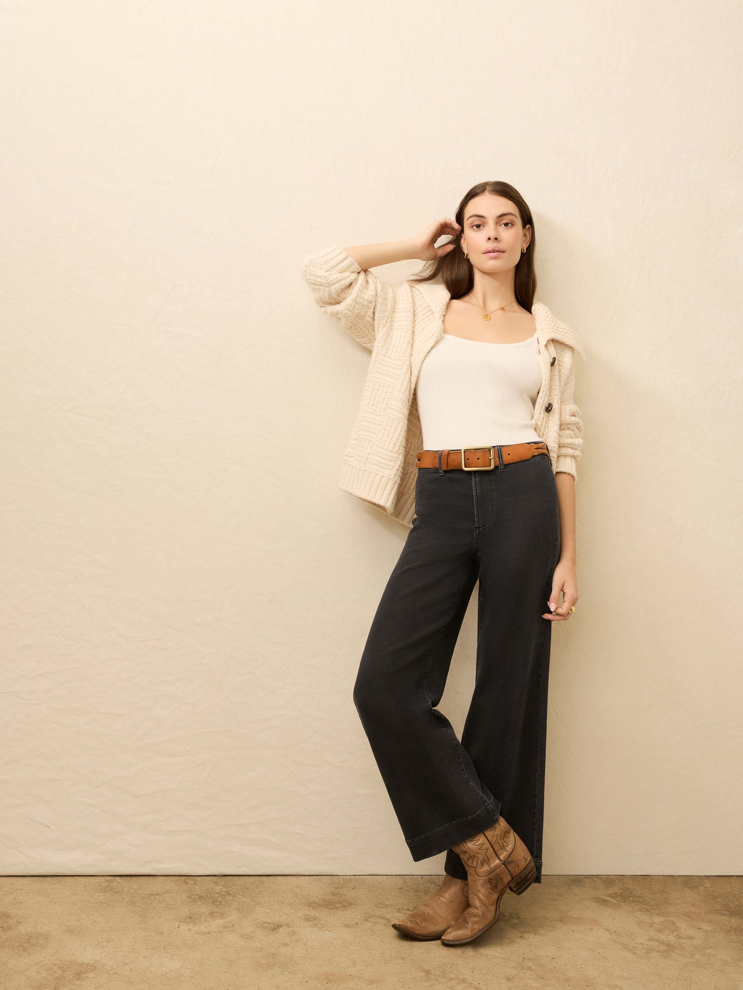 Woman wearing black wide-leg jeans and a white top against a beige background
