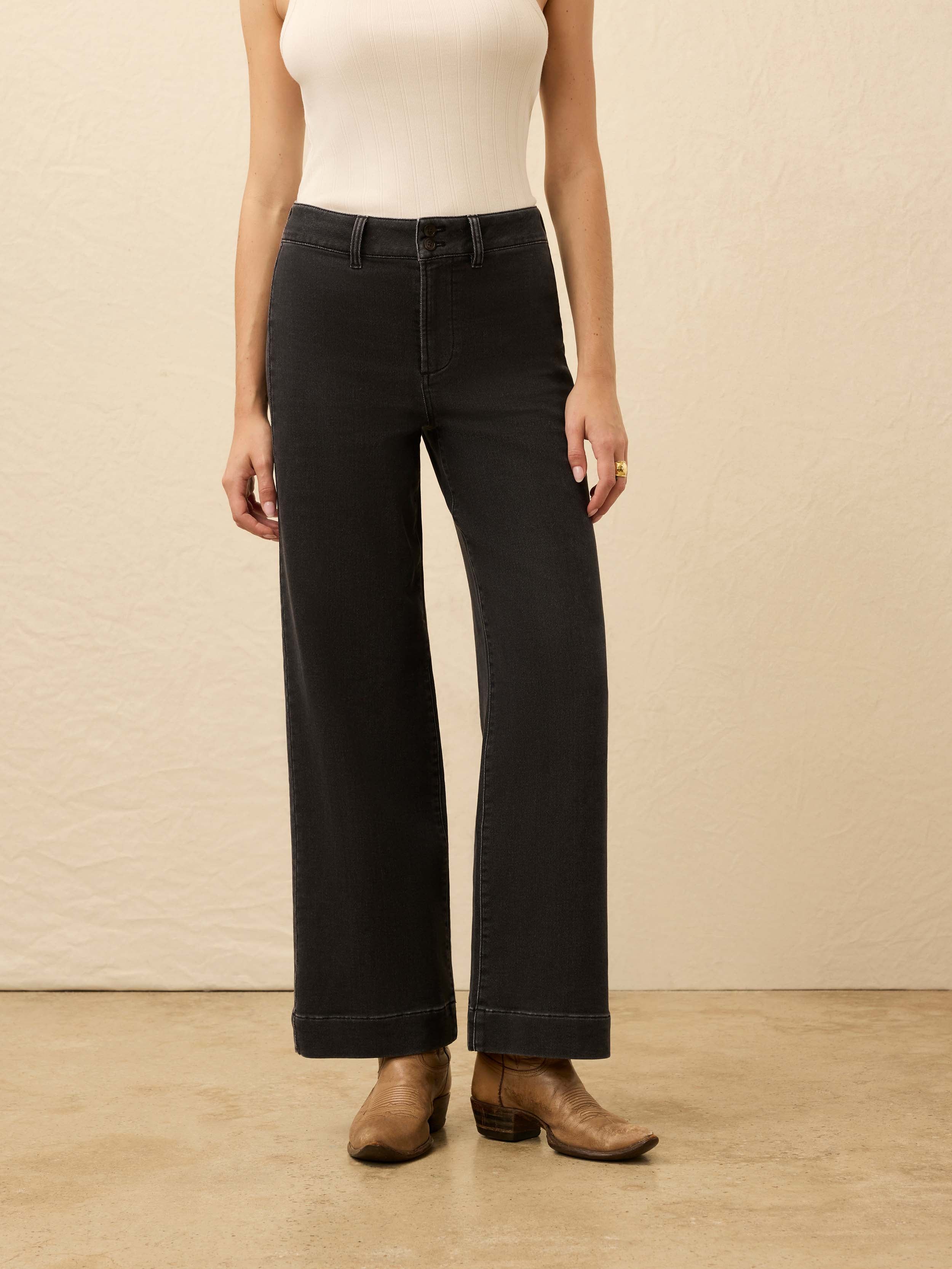 Woman wearing black wide-leg jeans and a white top against a beige background