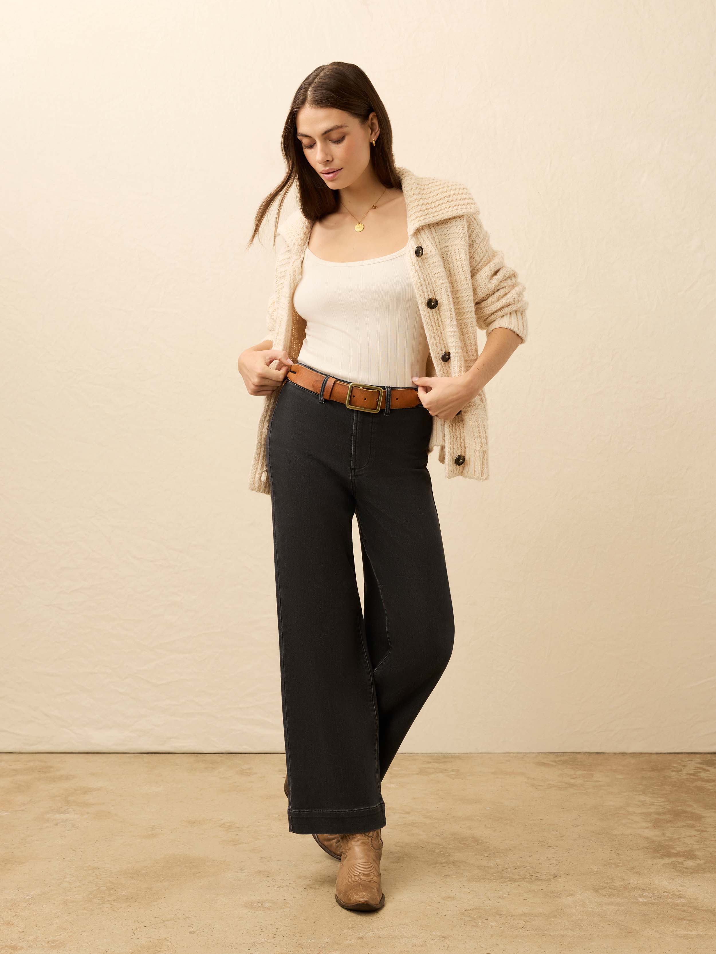 Woman wearing a white top, black pants, and a beige cardigan against a beige background