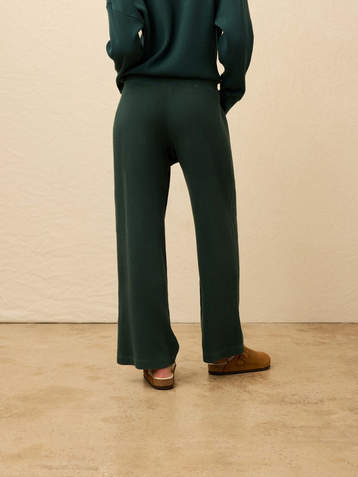 Woman is wearing green waffle pants with a matching henley long sleeve against a beige background, image 5 of 5