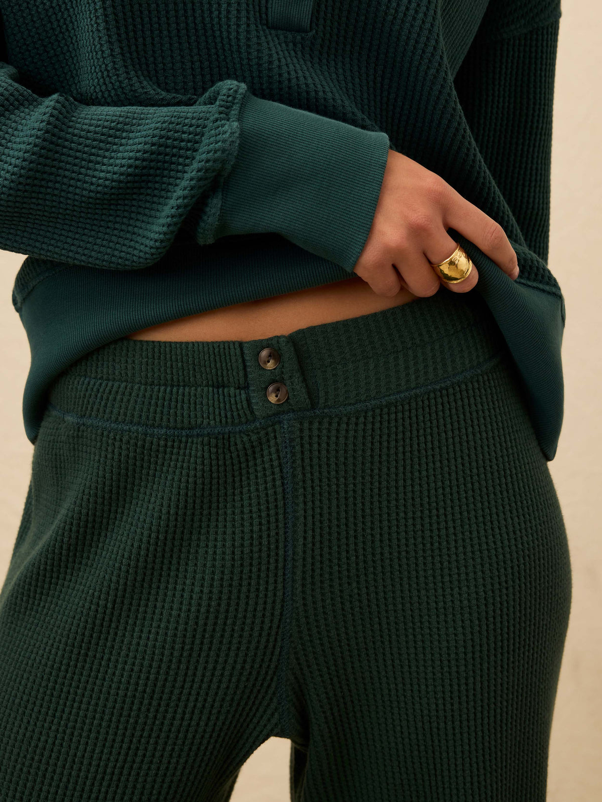 Woman is wearing green waffle pants with a matching henley long sleeve against a beige background, image 2 of 5