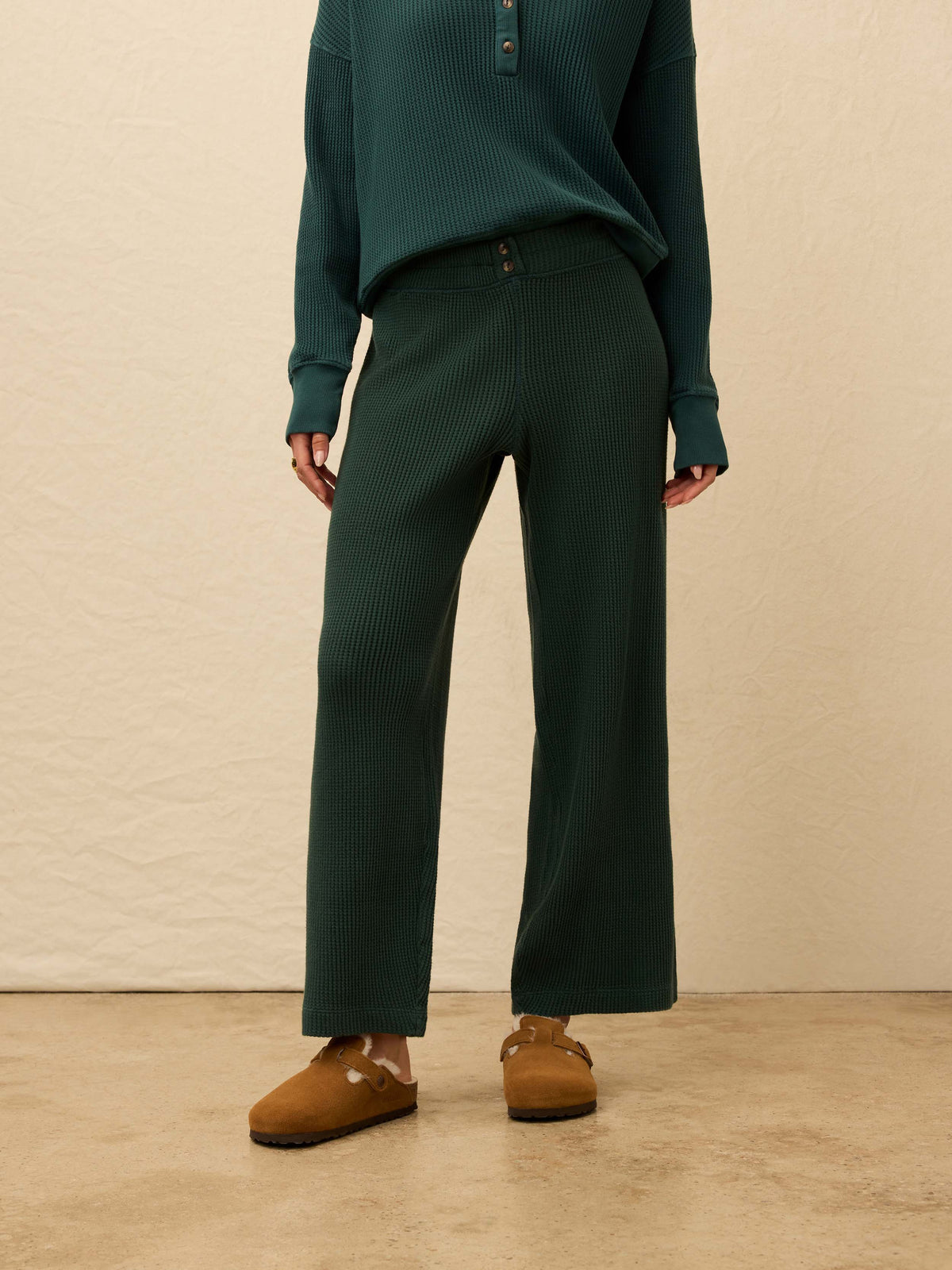 Woman is wearing green waffle pants with a matching henley long sleeve against a beige background, image 4 of 5