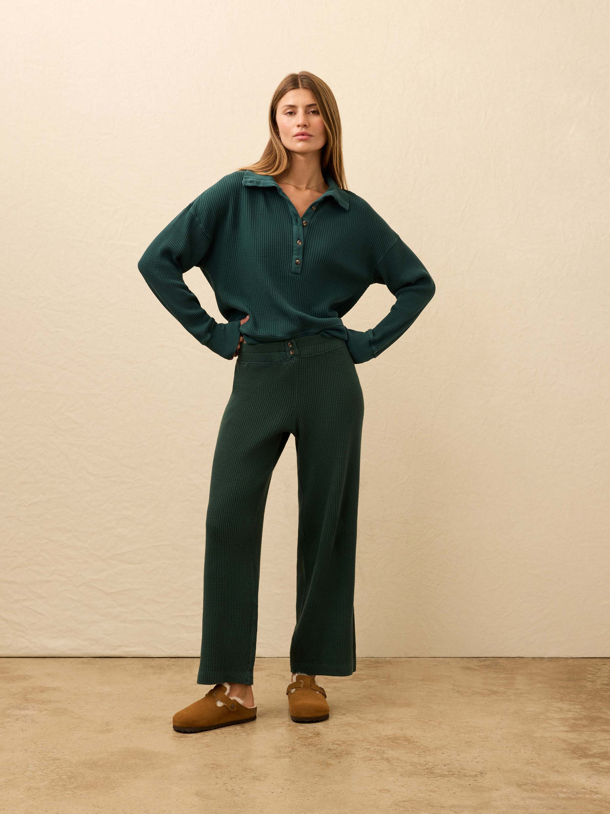 Woman is wearing green waffle pants with a matching henley long sleeve against a beige background, image 1 of 5