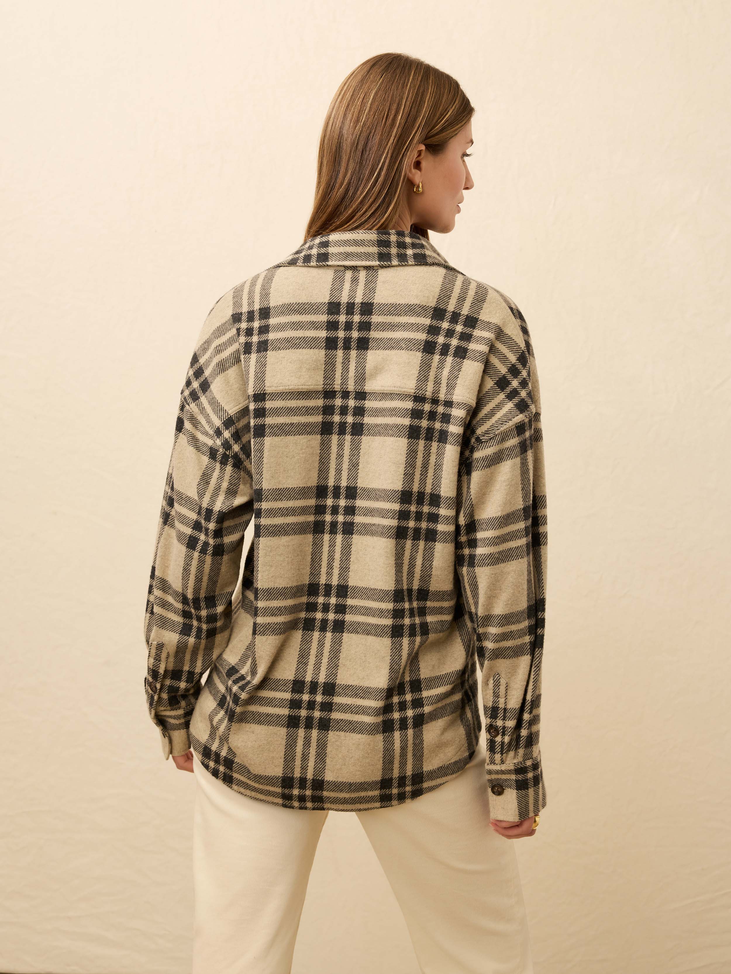 Woman is wearing a tan plaid shirt with white jeans against a beige background