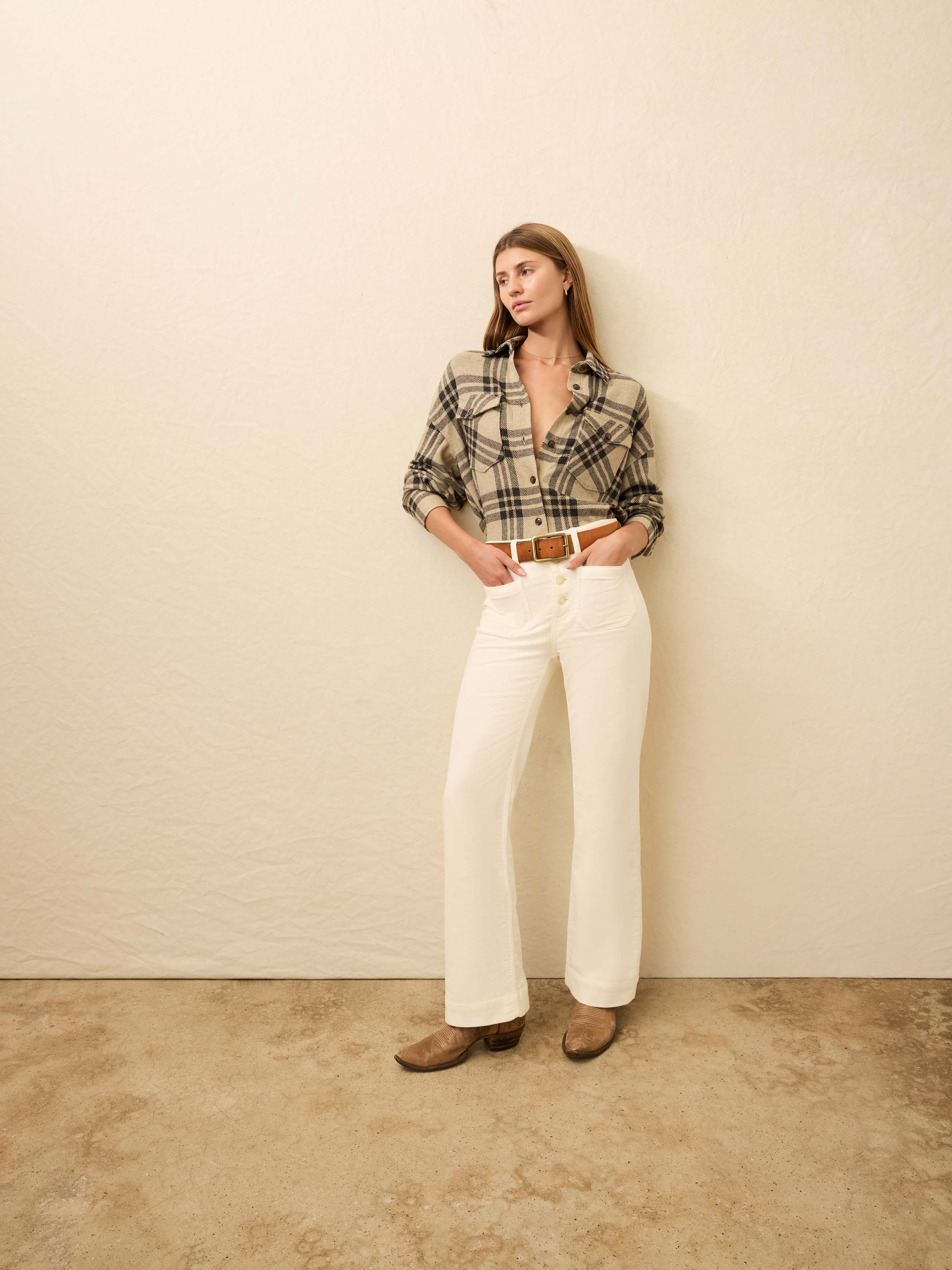 Woman is wearing a tan plaid shirt with white jeans against a beige background
