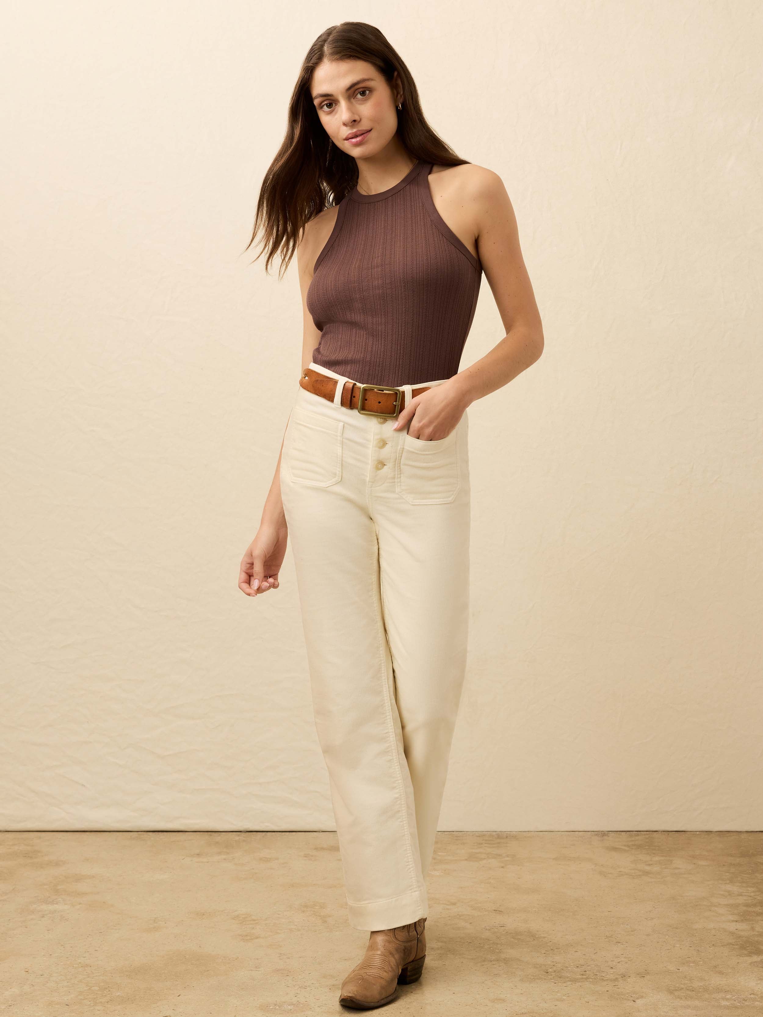 Woman wearing a brown top and white pants against a beige background