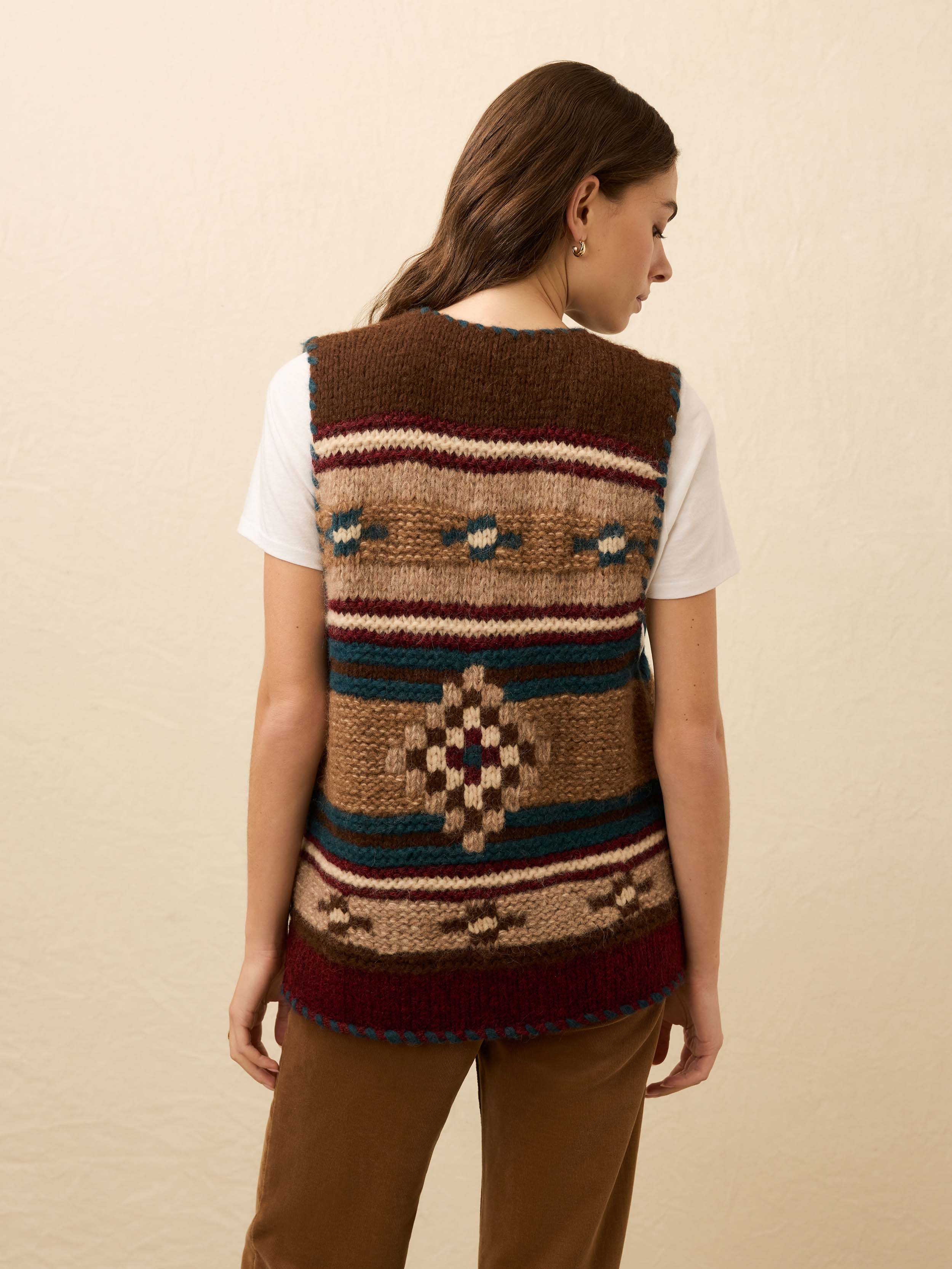 Woman wearing a hand knit patterned vest over a white tee shirt on a beige background