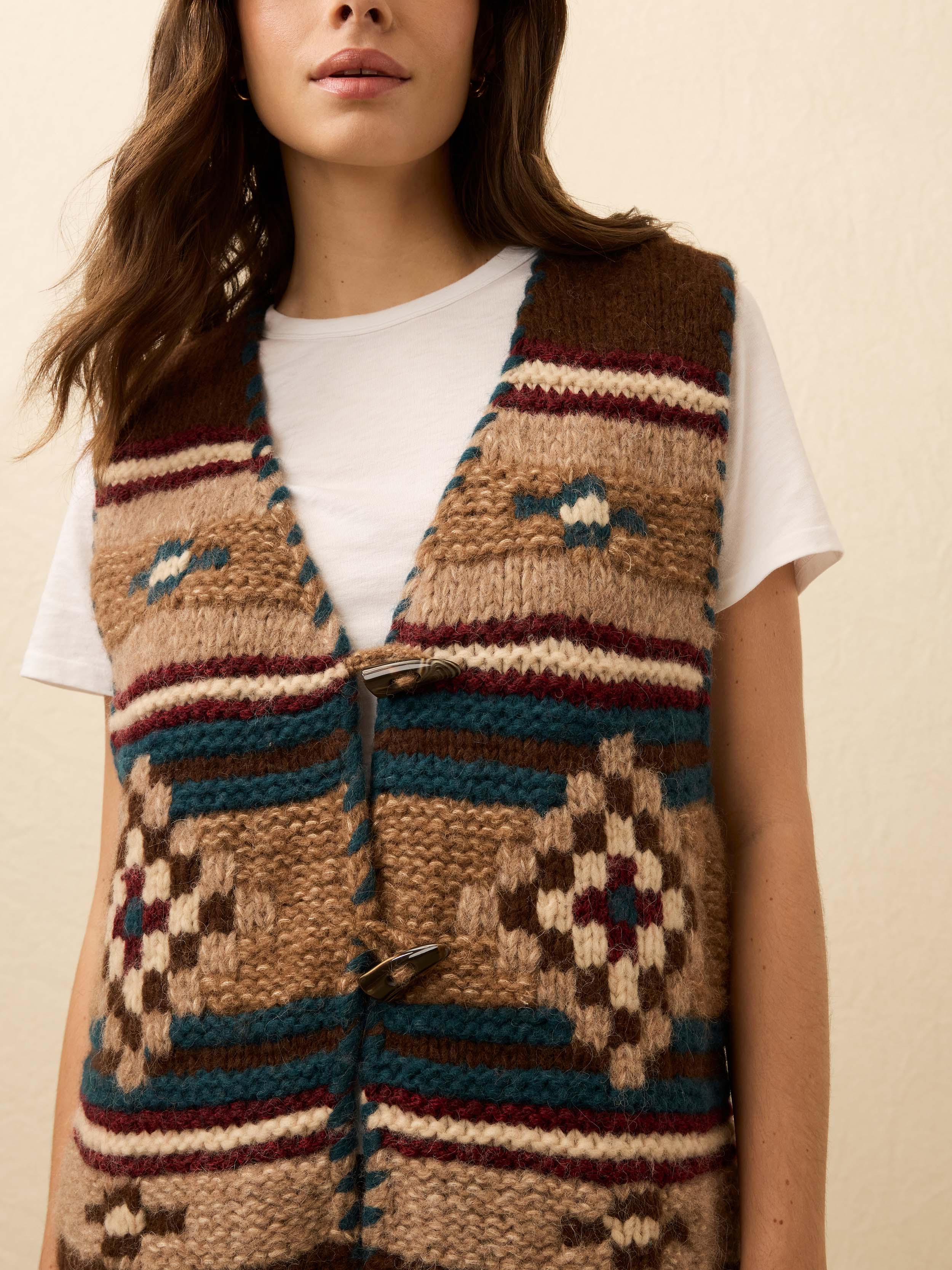 Woman wearing a hand knit patterned vest over a white tee shirt on a beige background