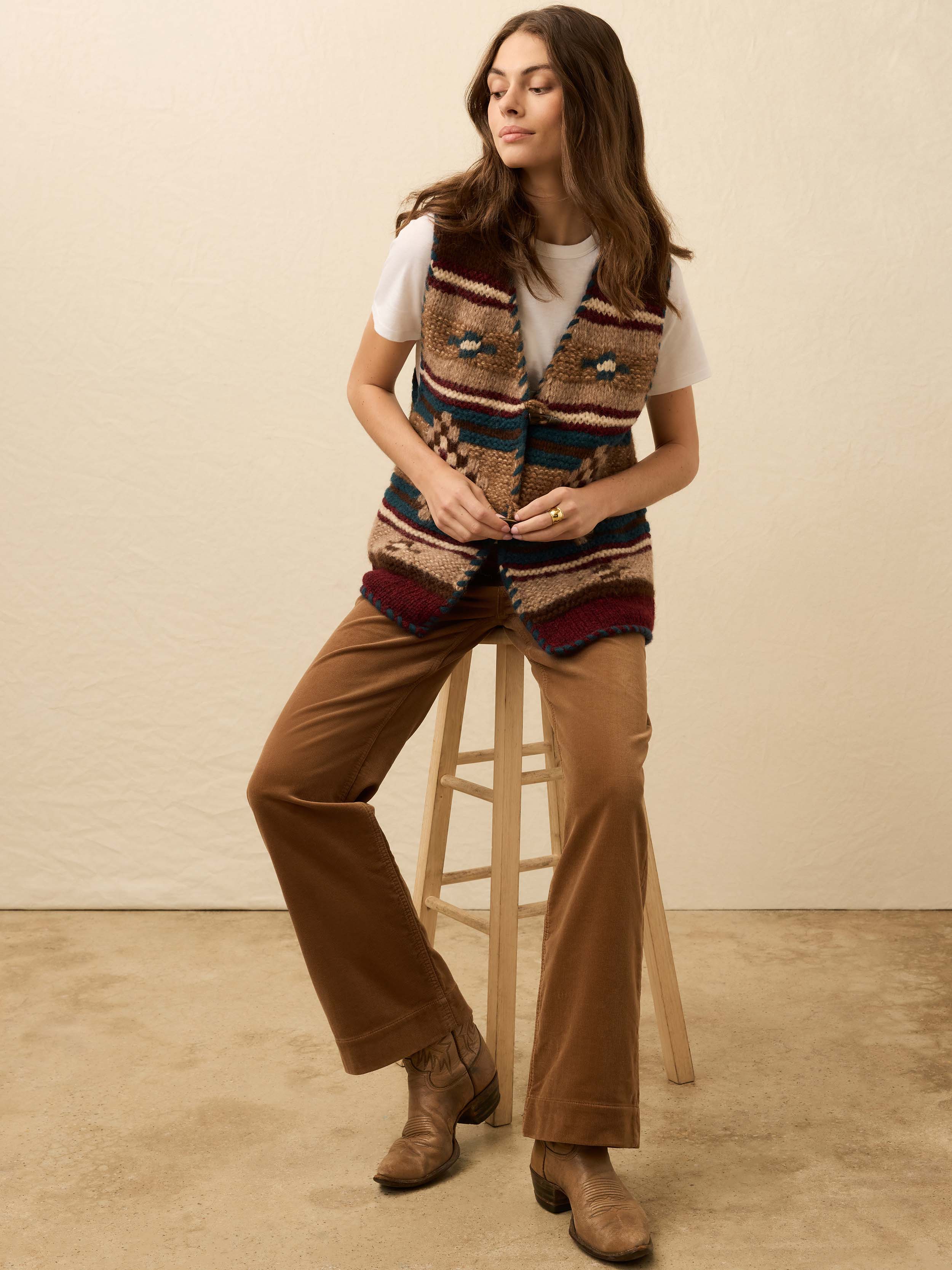 Woman wearing a hand knit patterned vest over a white tee shirt on a beige background