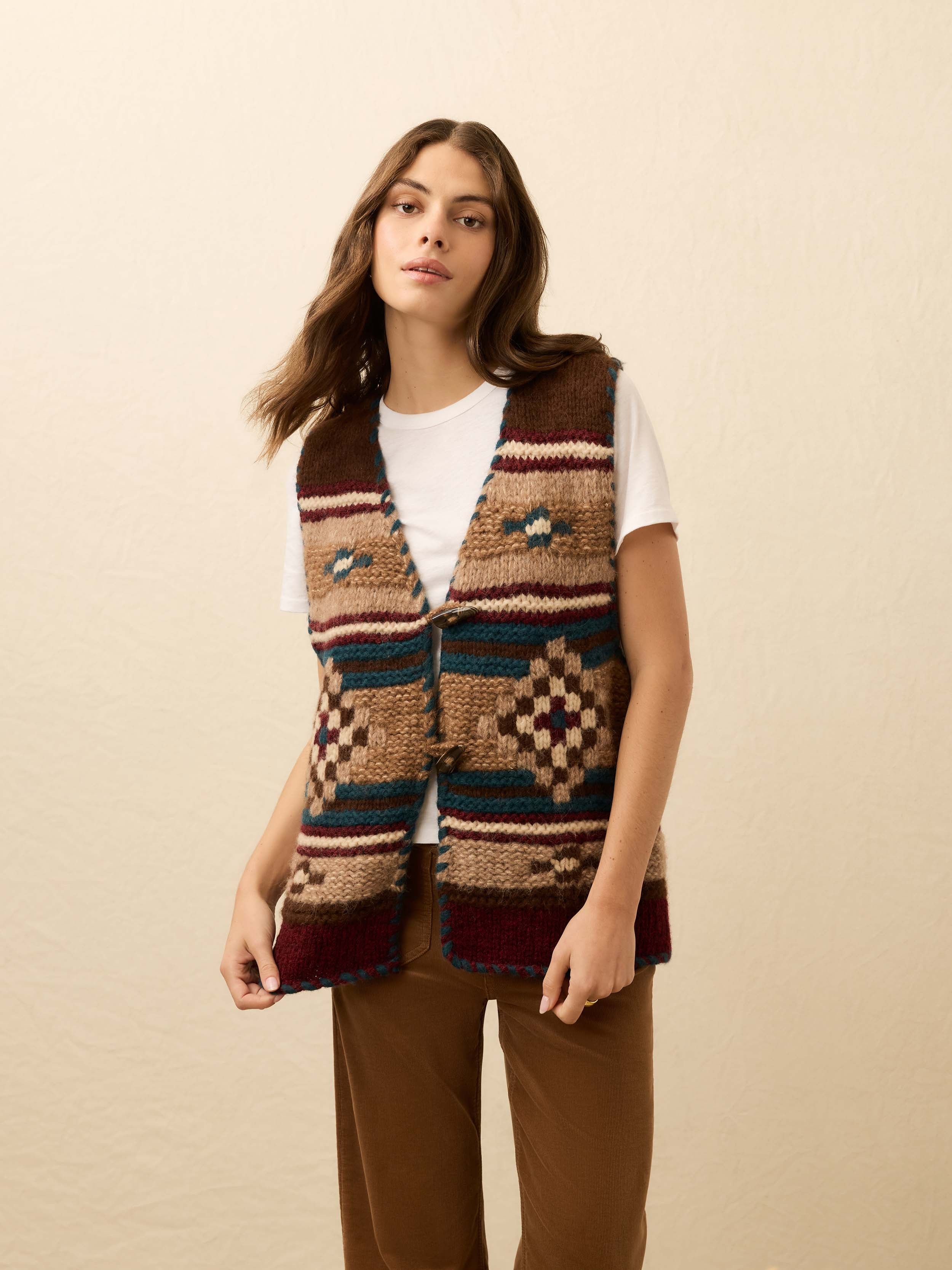 Woman wearing a hand knit patterned vest over a white tee shirt on a beige background
