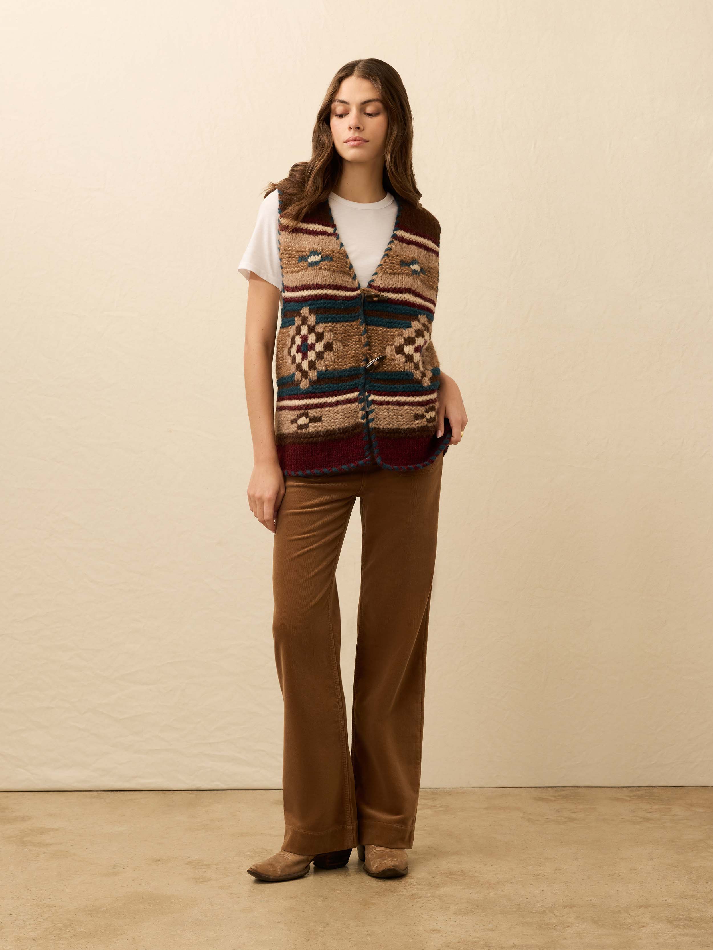 Woman wearing a hand knit patterned vest over a white tee shirt on a beige background