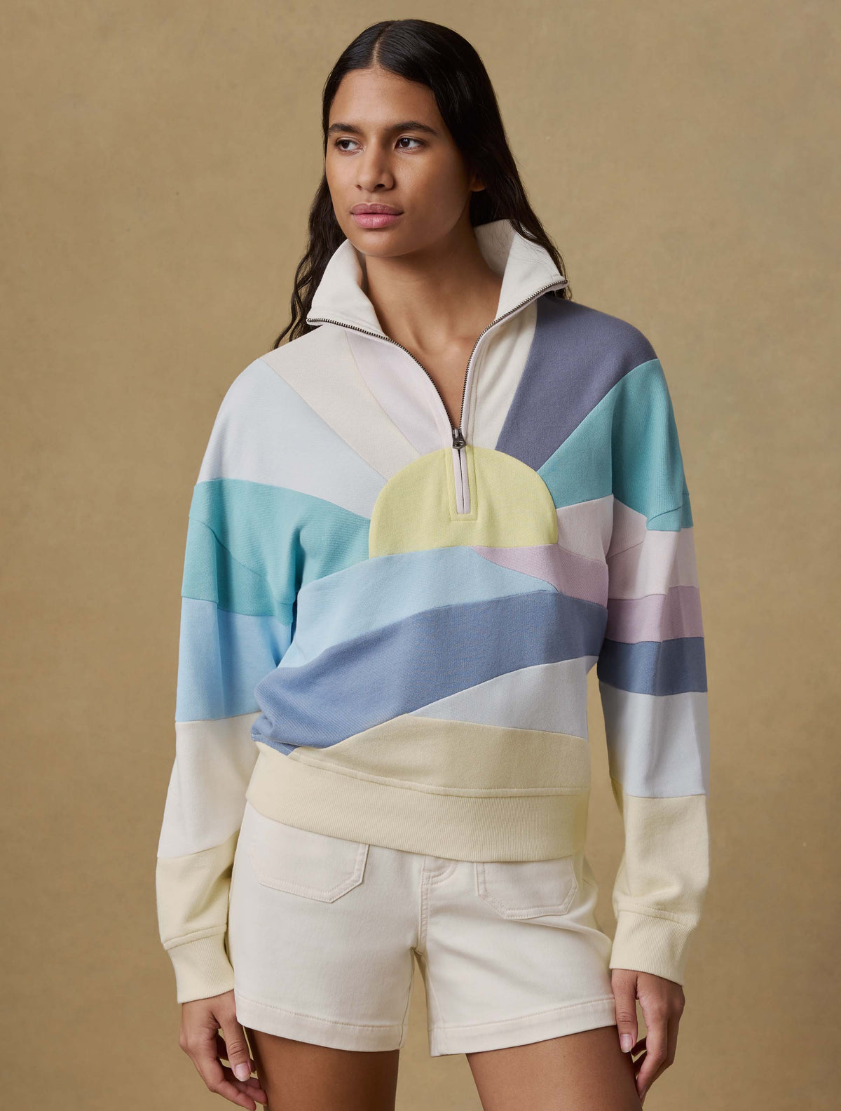 Woman wearing a colorful striped sweater and white shorts against a beige background, image 4 of 6