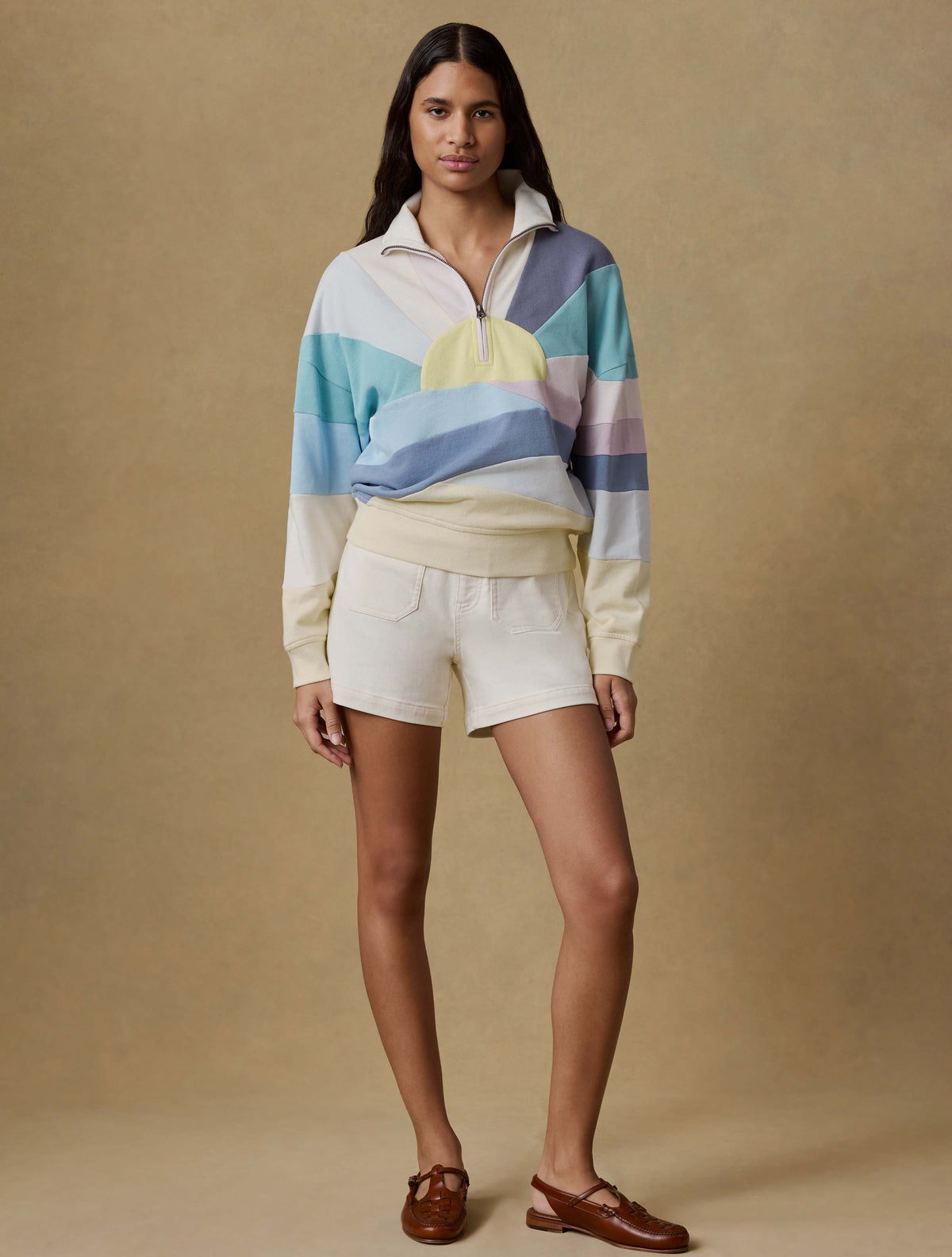 Woman wearing a colorful striped sweater and white shorts against a beige background, image 2 of 6