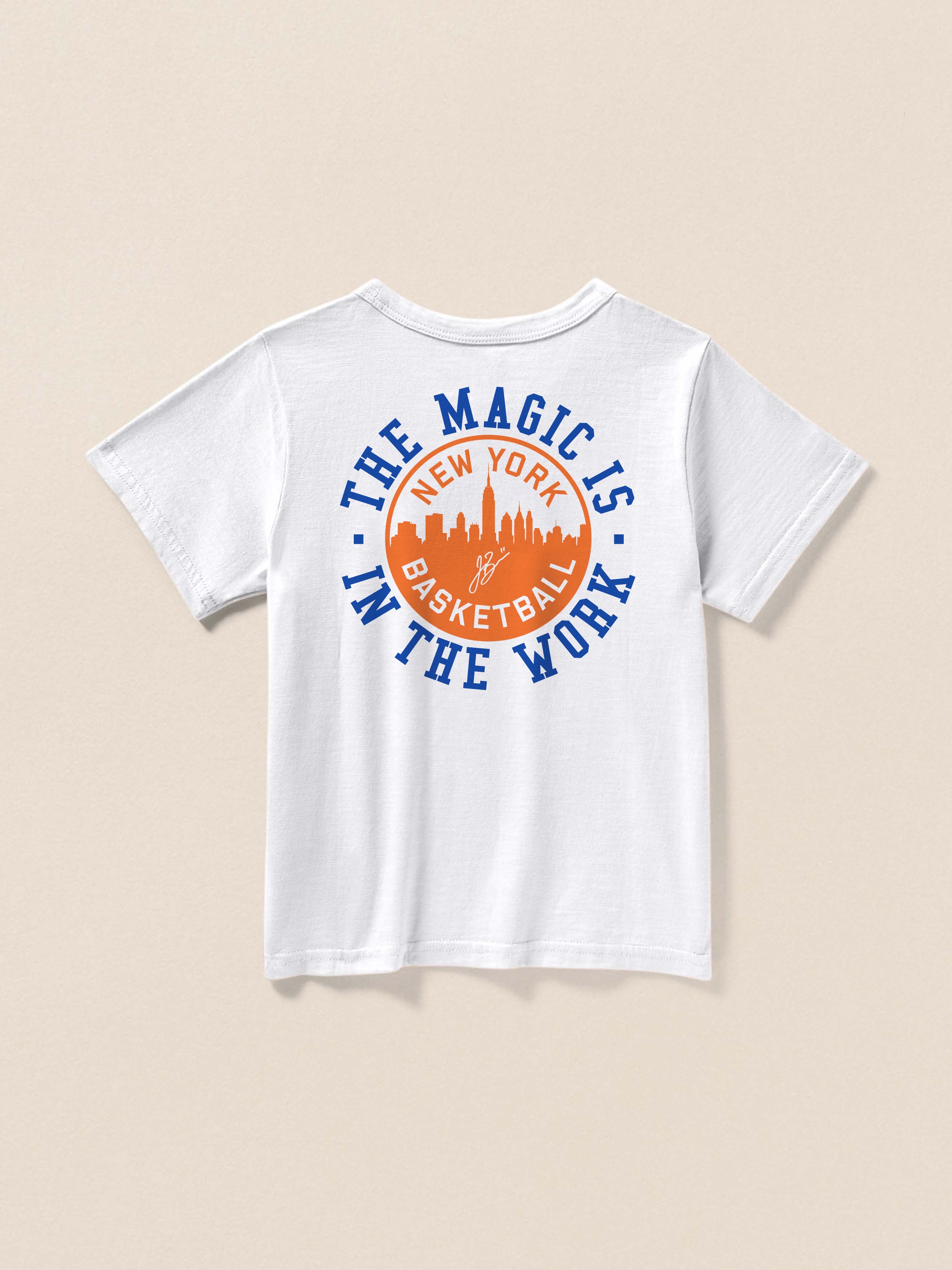 White t-shirt with a "Magic Is In The Work" graphic on the back against a beige background