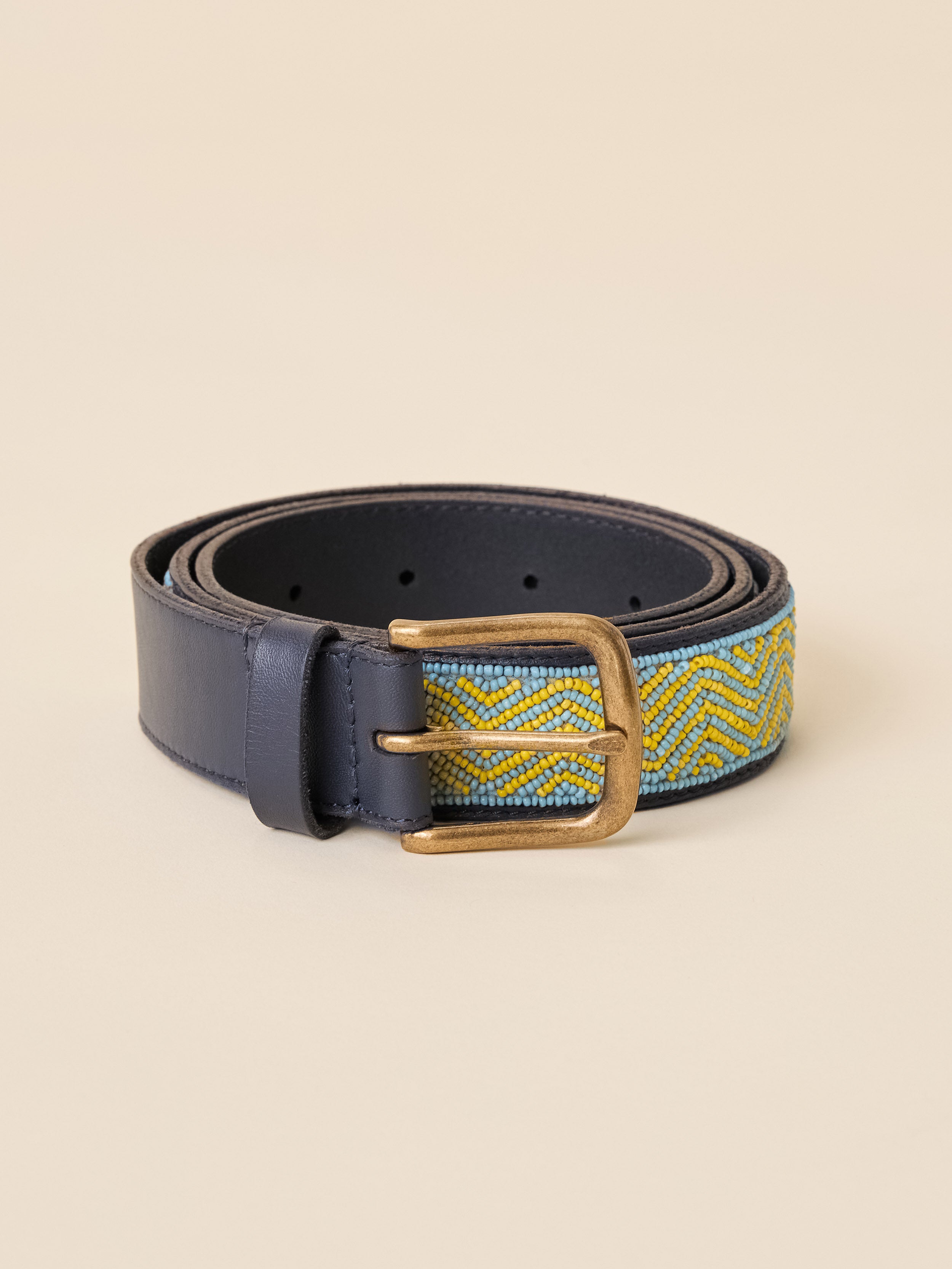 A navy blue leather belt with a woven chevron pattern in yellow and light blue, featuring a gold-tone metal buckle, displayed on a solid beige background.