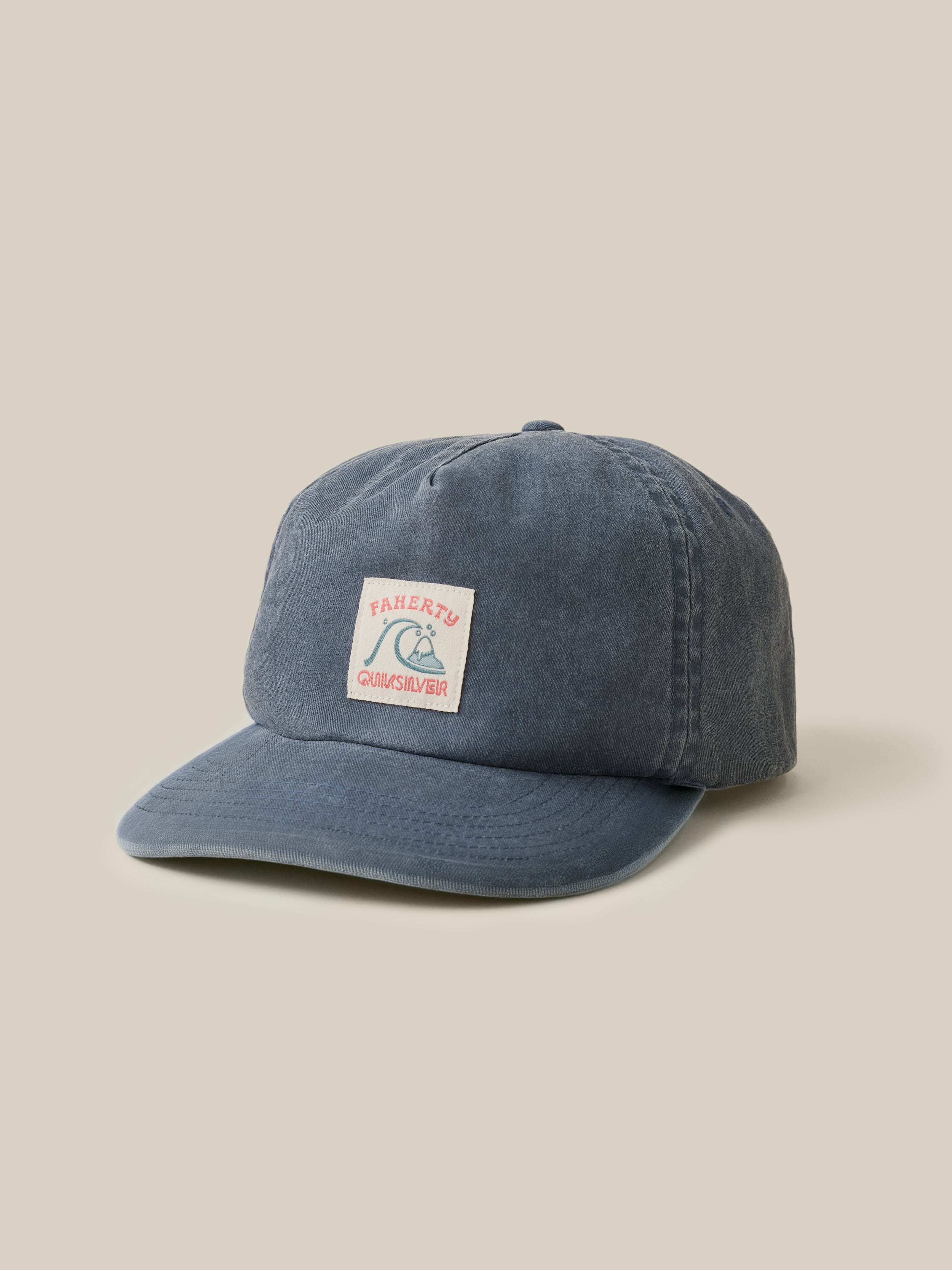 Blue cap with a Faherty x Quiksilver graphic on the center front on a beige background