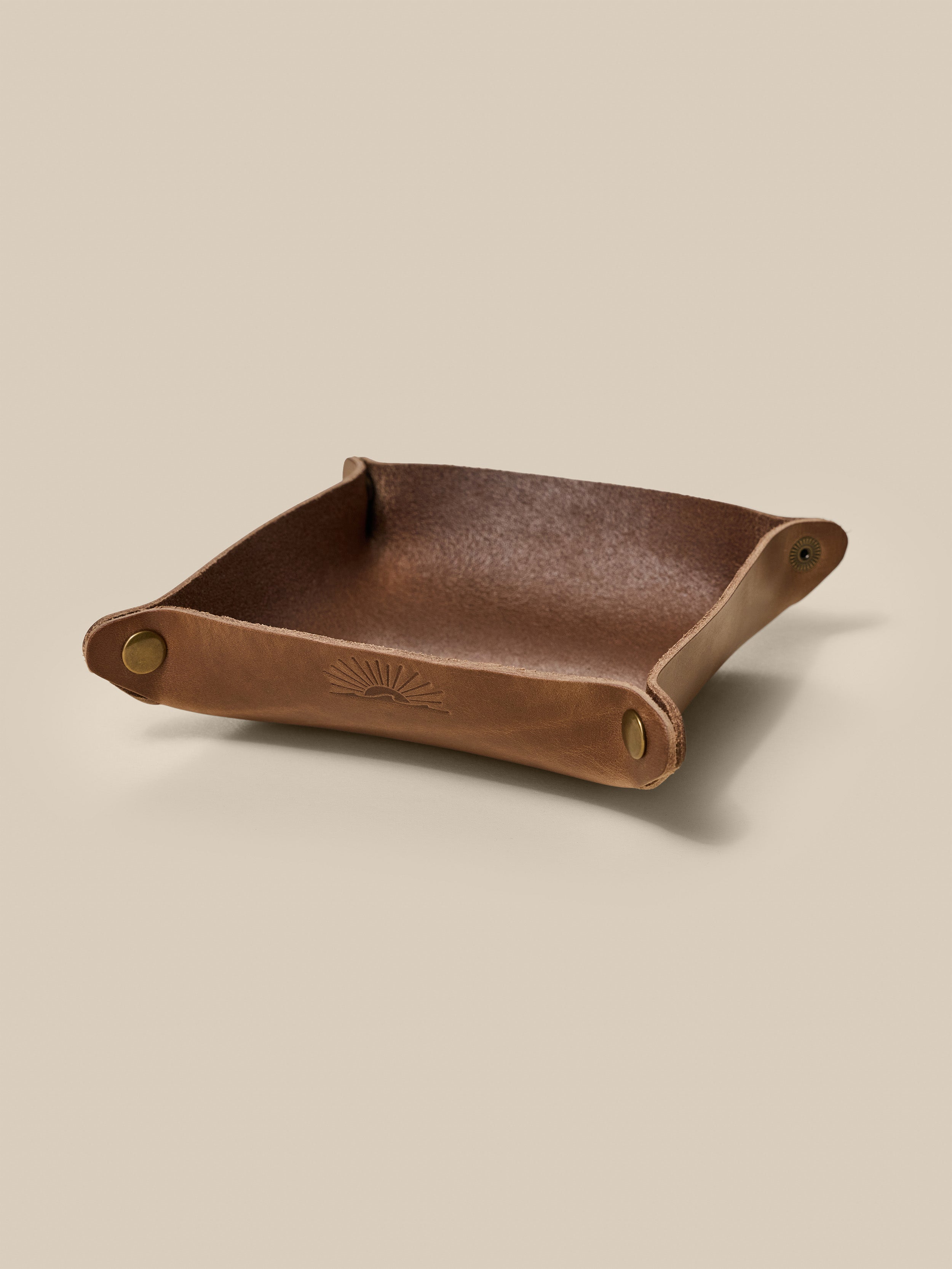 Brown leather tray with a subtle embossed Faherty logo on a beige background