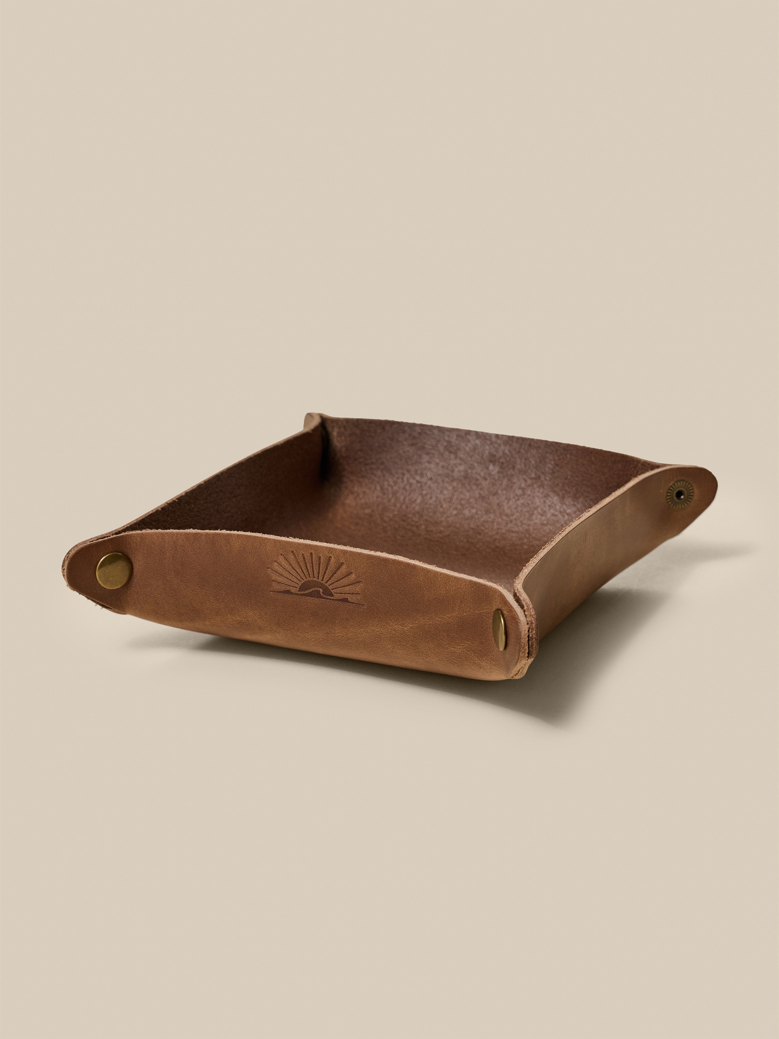 Brown leather tray with a subtle embossed Faherty logo on a beige background