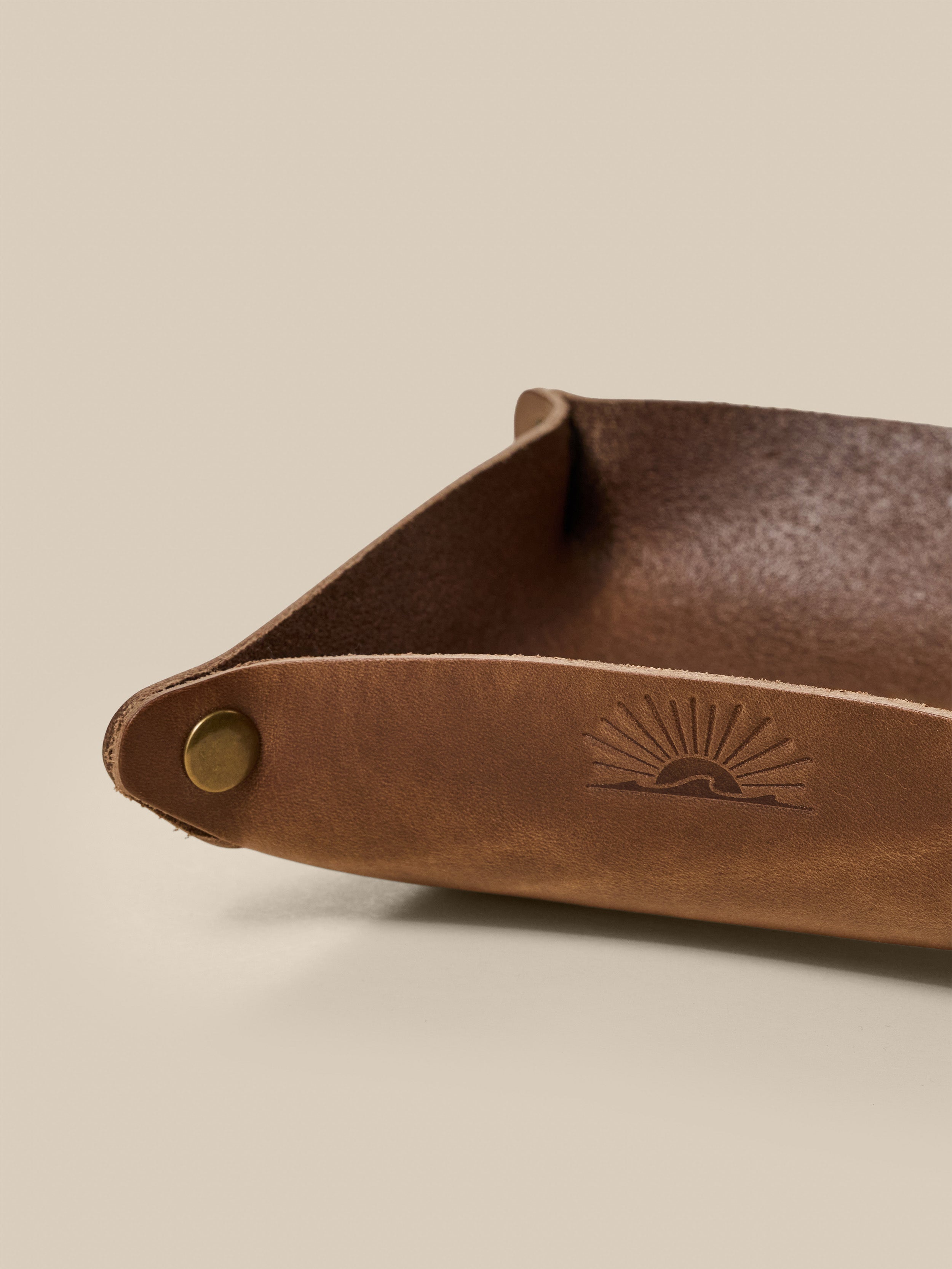 Brown leather tray with a subtle embossed Faherty logo on a beige background