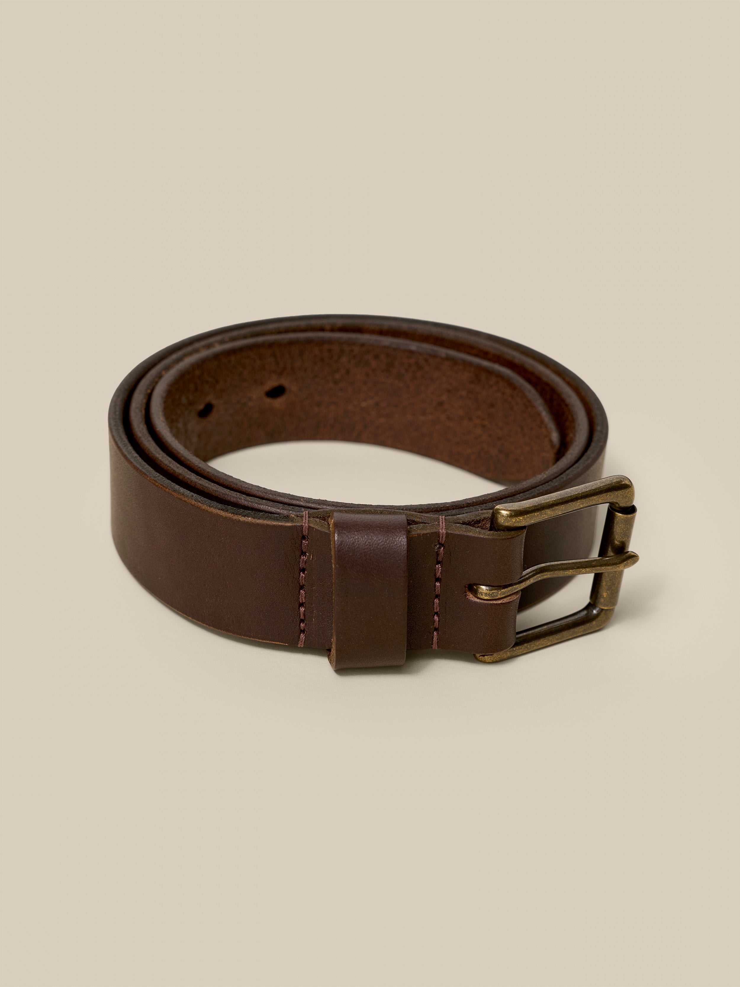 Brown leather belt with brass buckle on a beige background