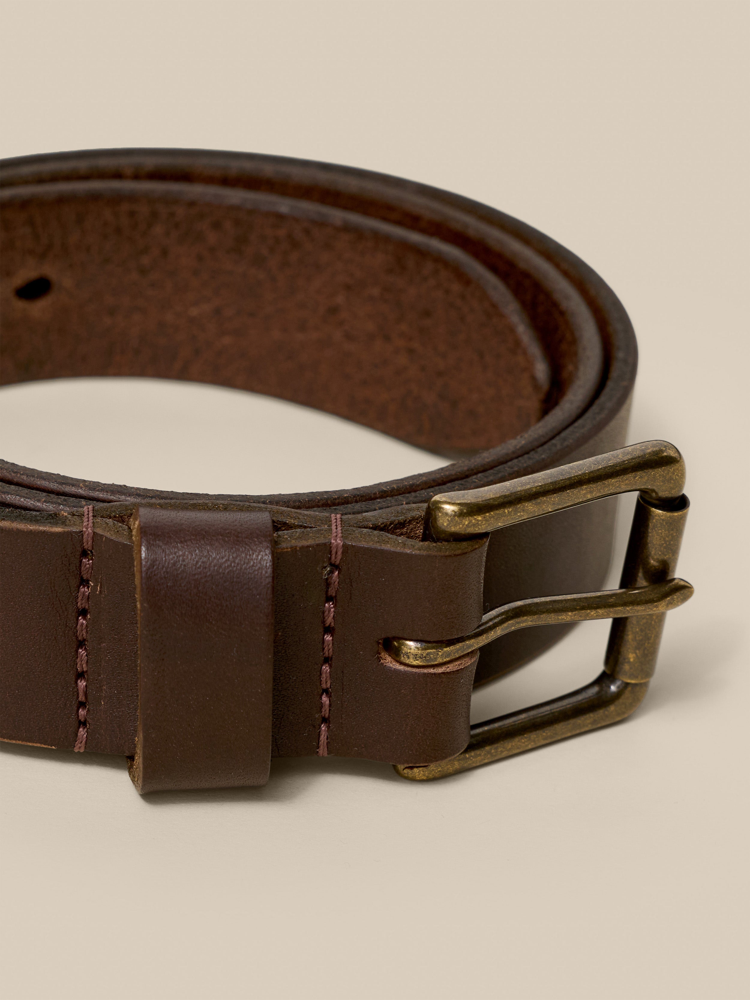 Brown leather belt with brass buckle on a beige background