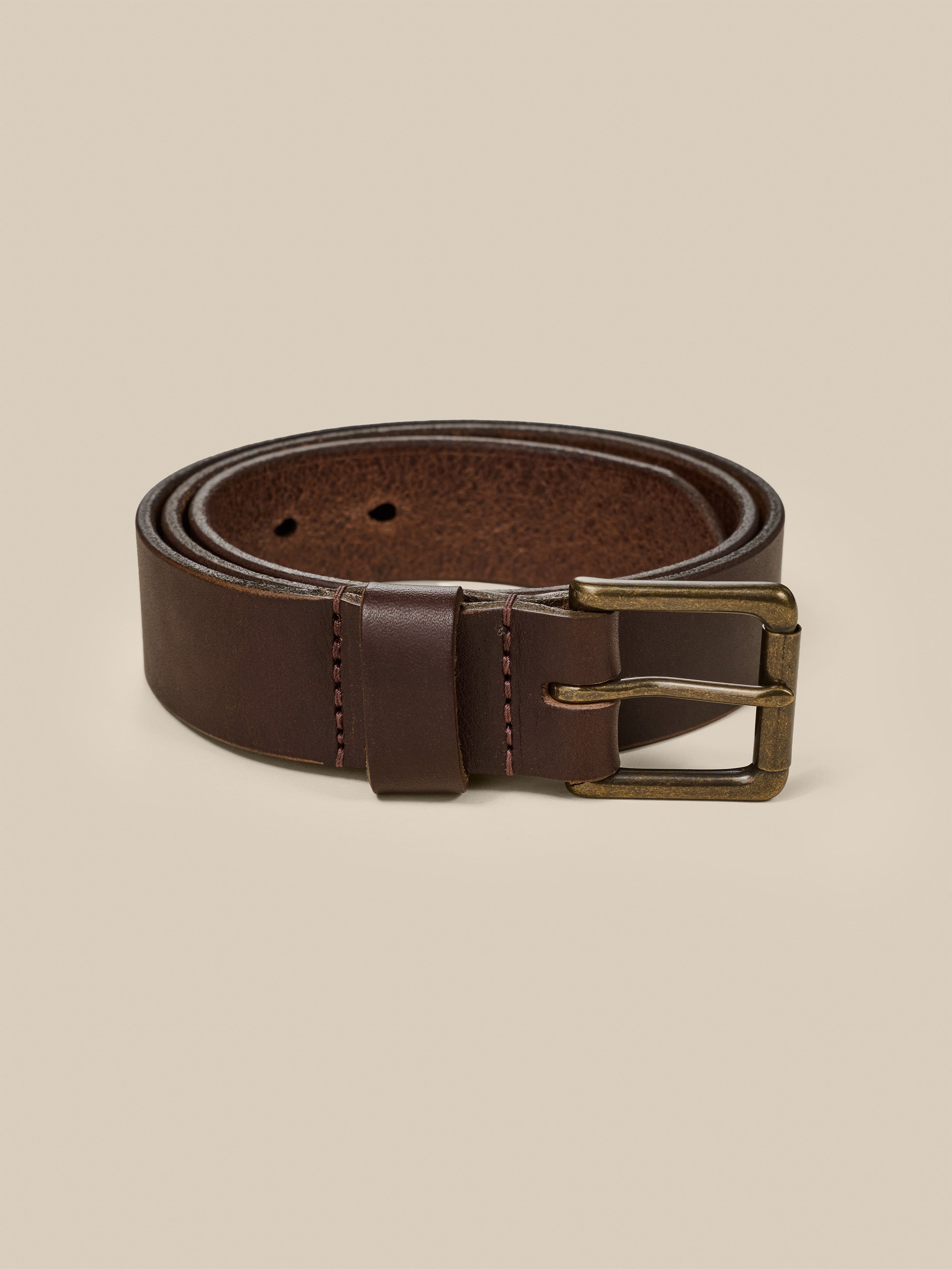 Brown leather belt with a brass buckle on a beige background