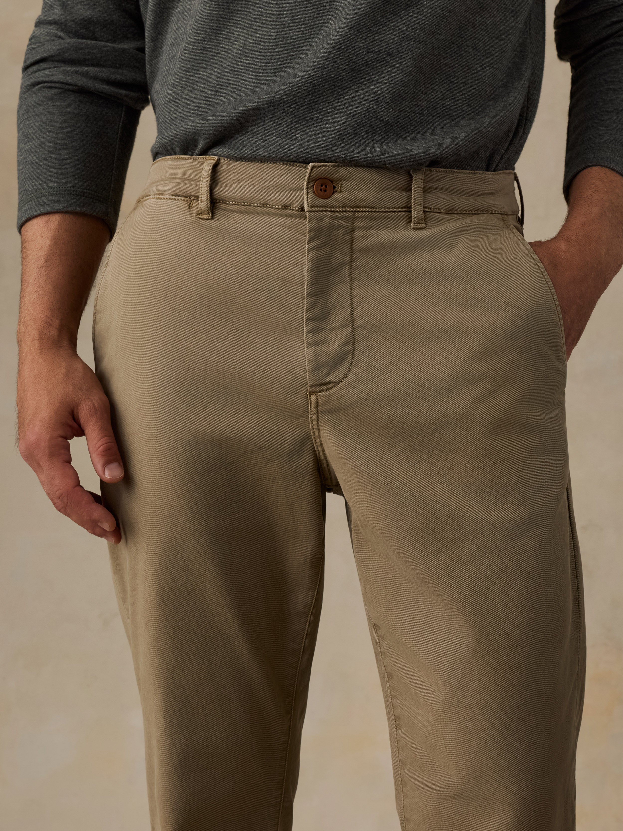 A close-up of a man wearing khaki chinos with a dark gray long-sleeve shirt, showing the front waistband, belt loops, and front pockets.