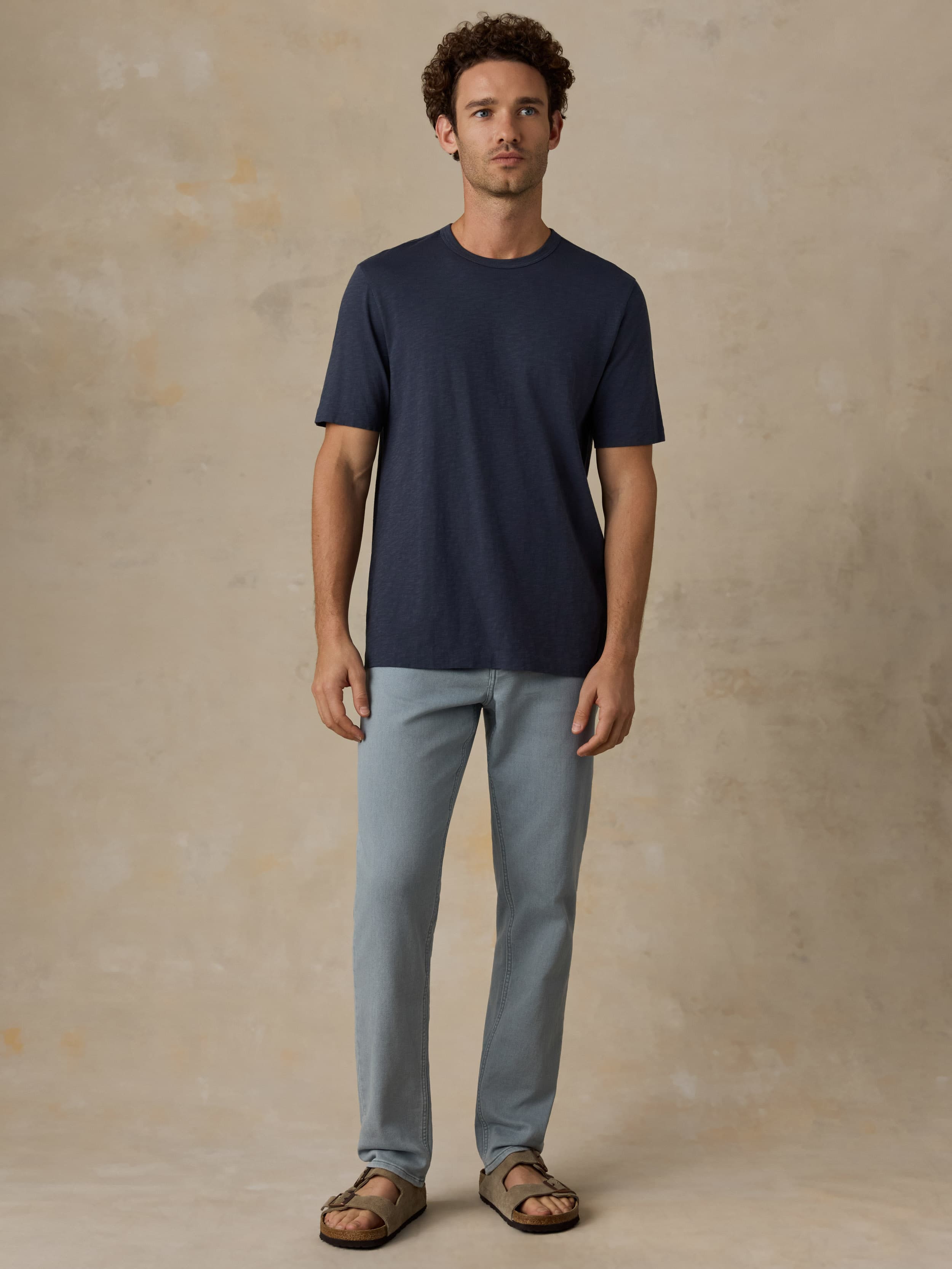 Man wearing a navy t-shirt and light blue pants against a beige background