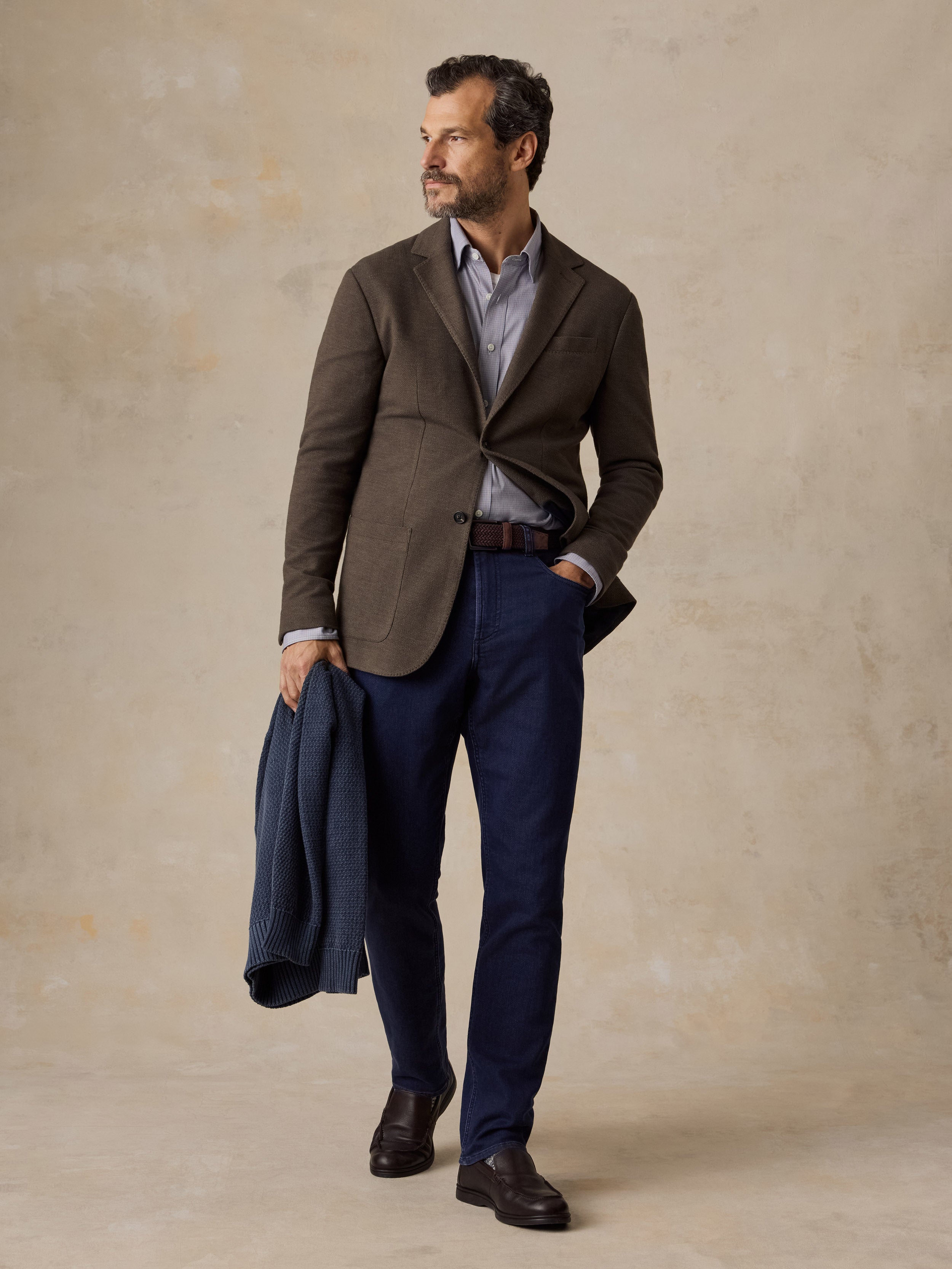 A man wearing a brown blazer, blue jeans, and leather shoes
