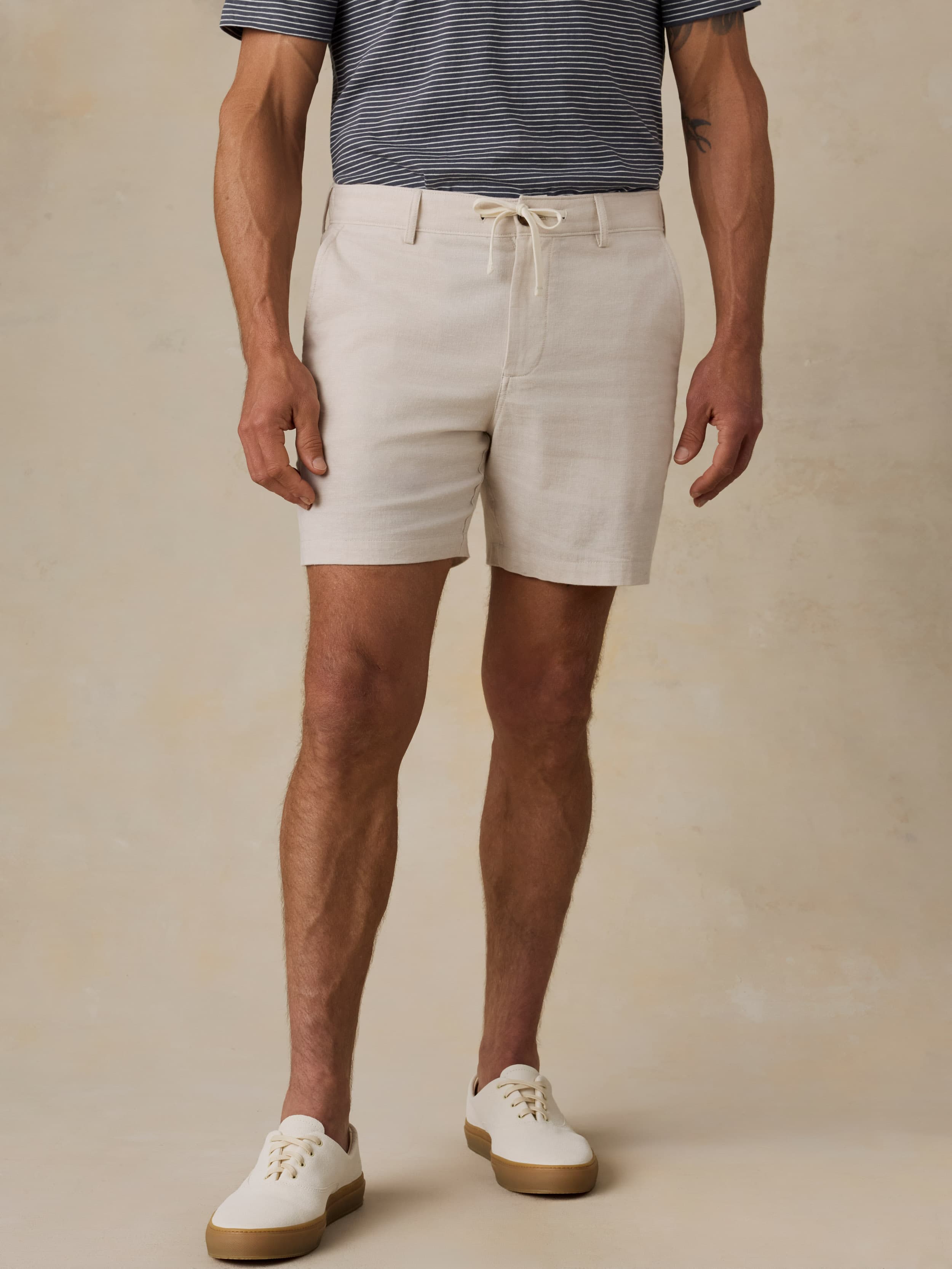Man wearing beige shorts and a striped shirt on a beige background