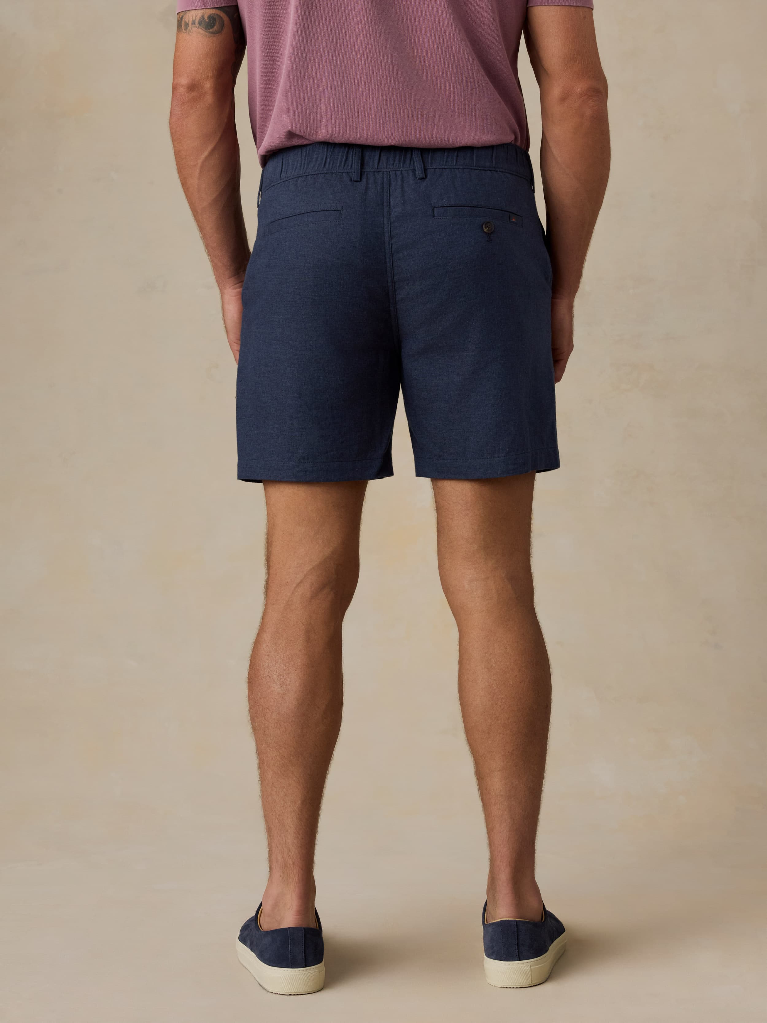 Man wearing navy shorts and a purple shirt on a beige background