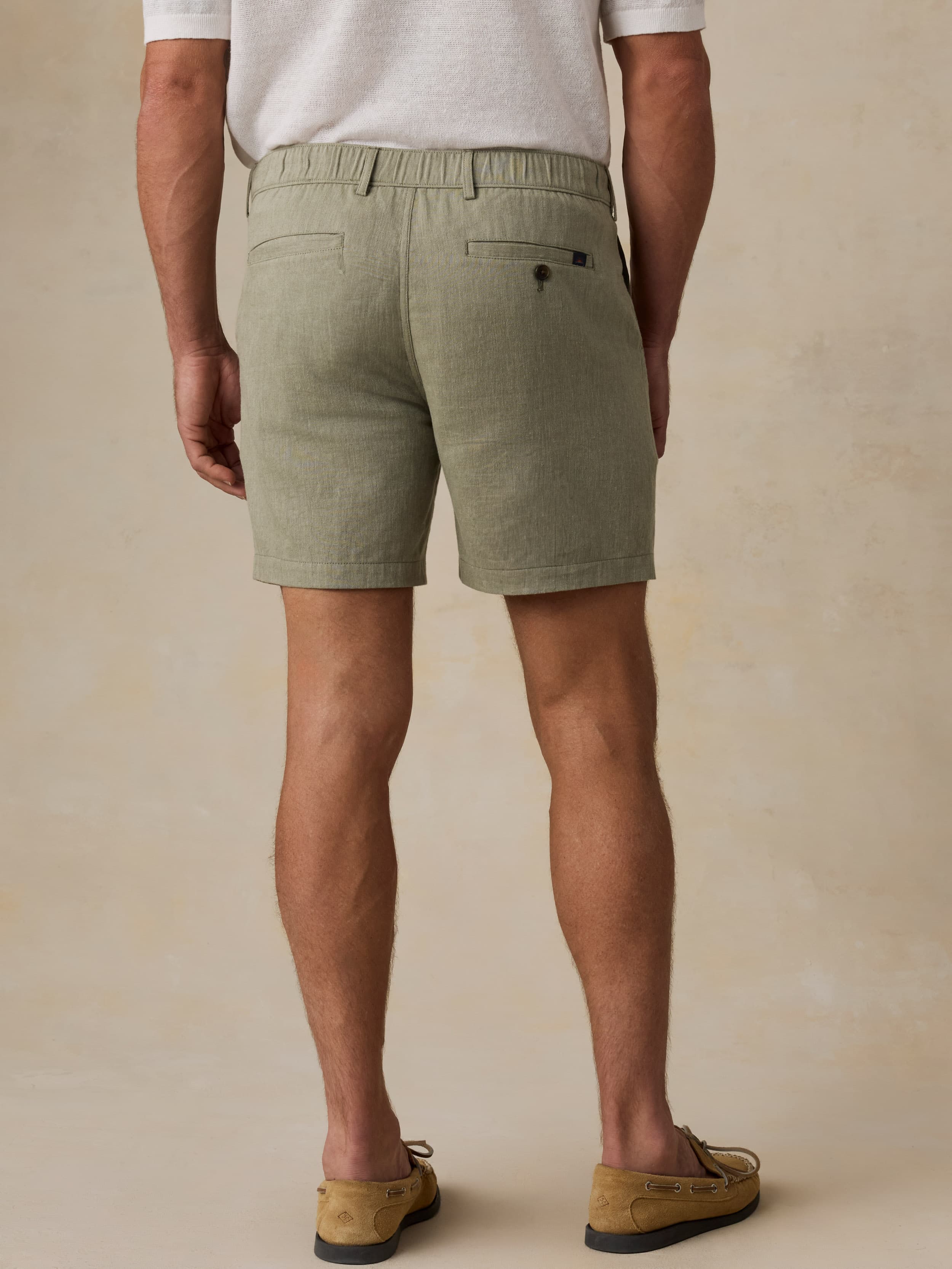 Man wearing a white polo shirt and green linen shorts against a beige background