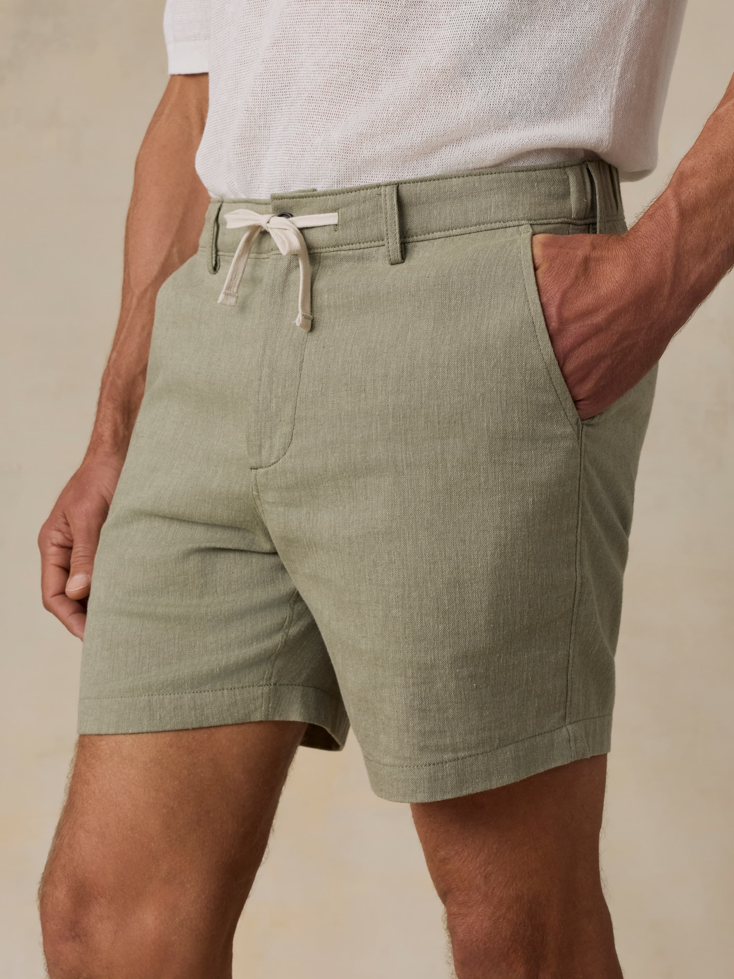 Man wearing a white polo shirt and green linen shorts against a beige background