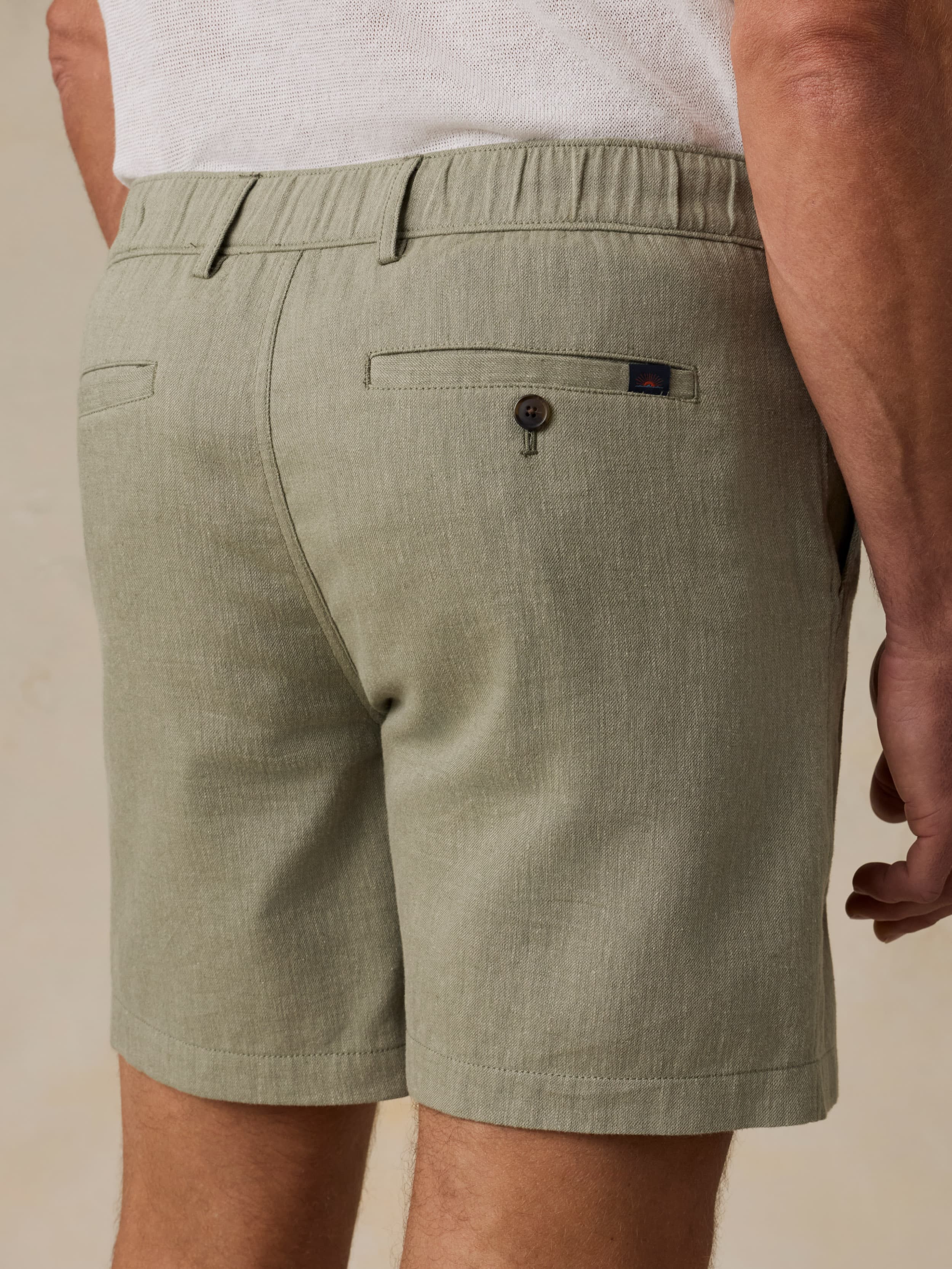 Man wearing a white polo shirt and green linen shorts against a beige background