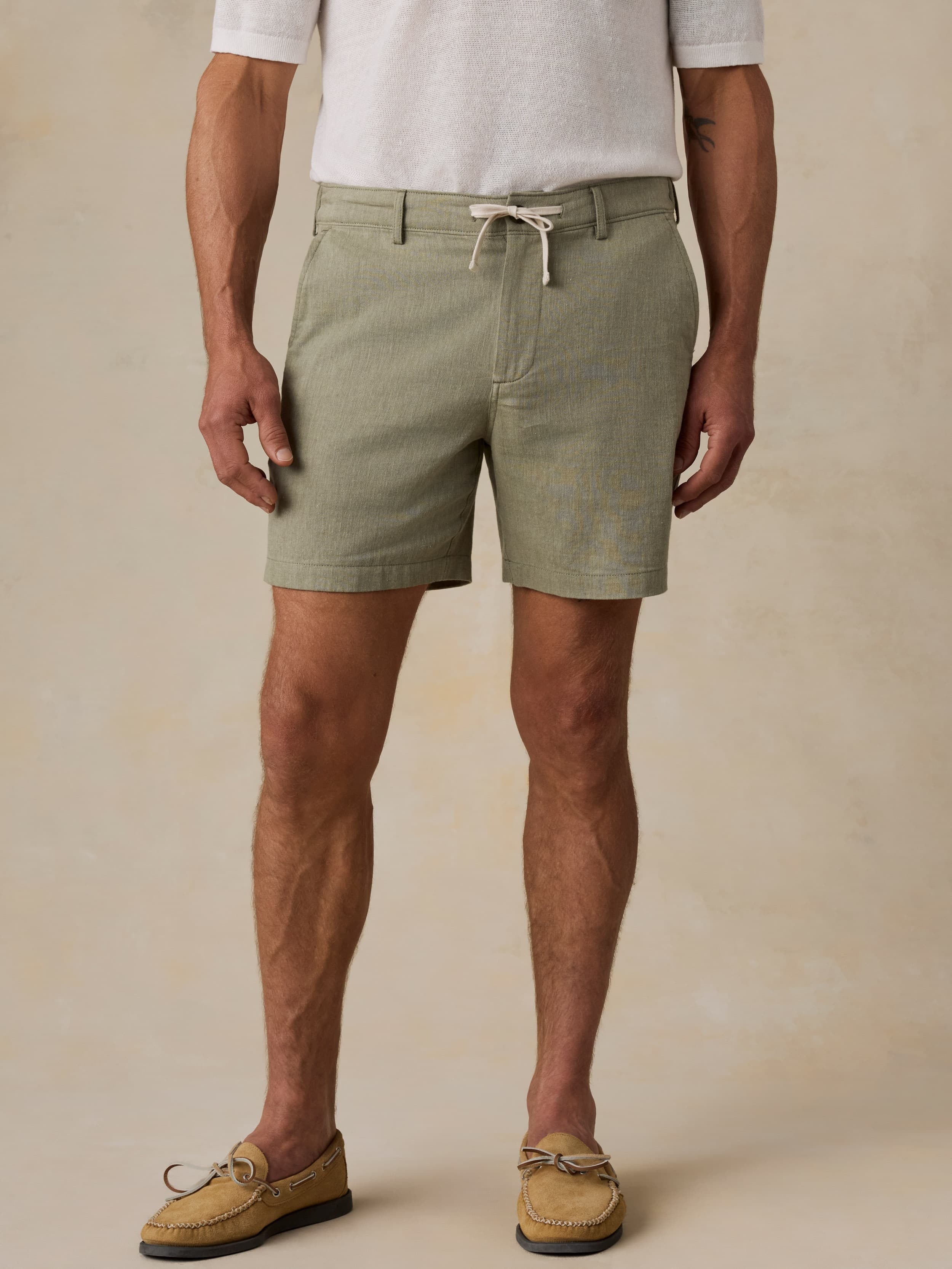 Man wearing a white polo shirt and green linen shorts against a beige background