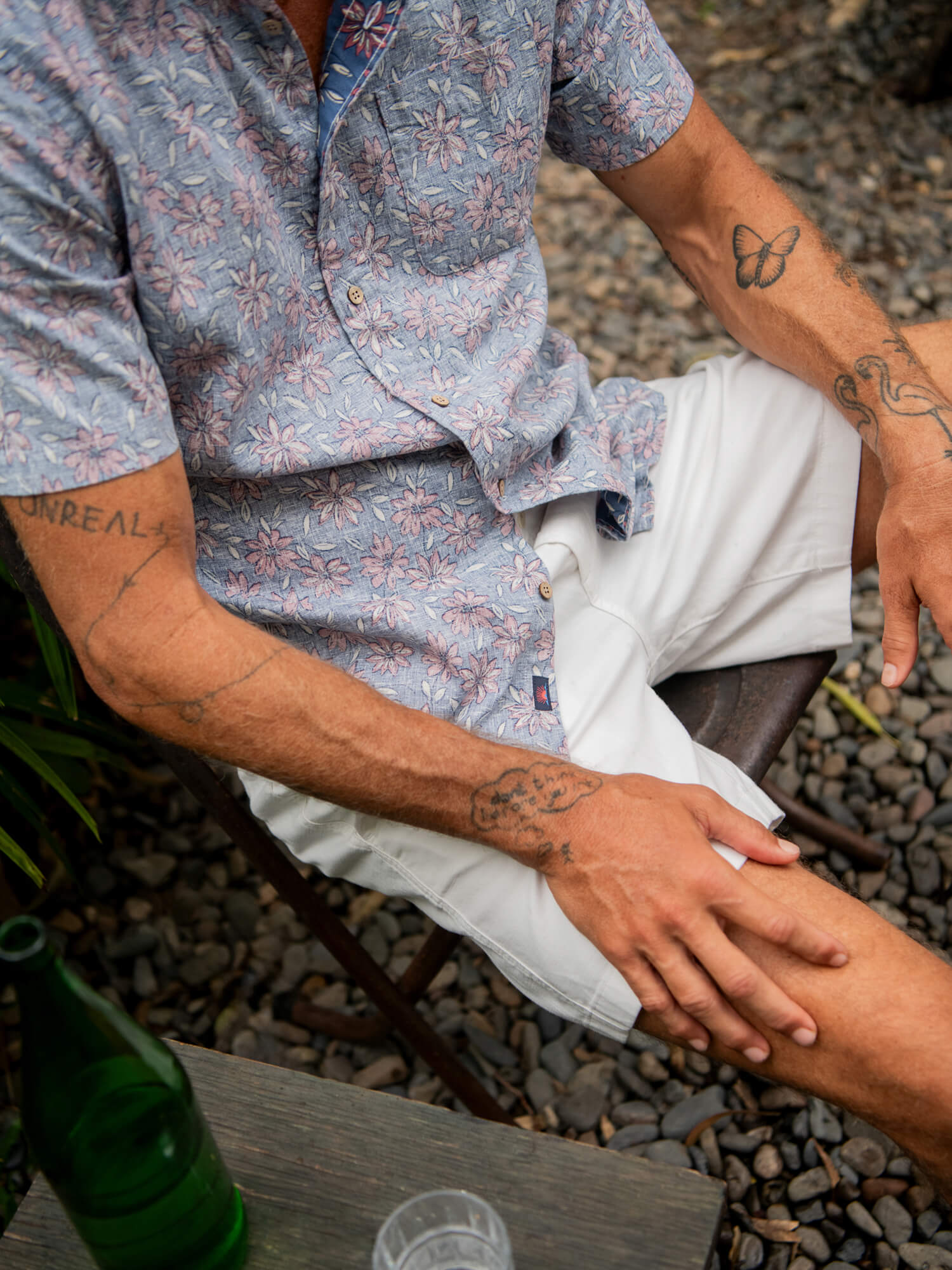 Man wearing a floral printed shirt and white shorts sitting on a chair outside