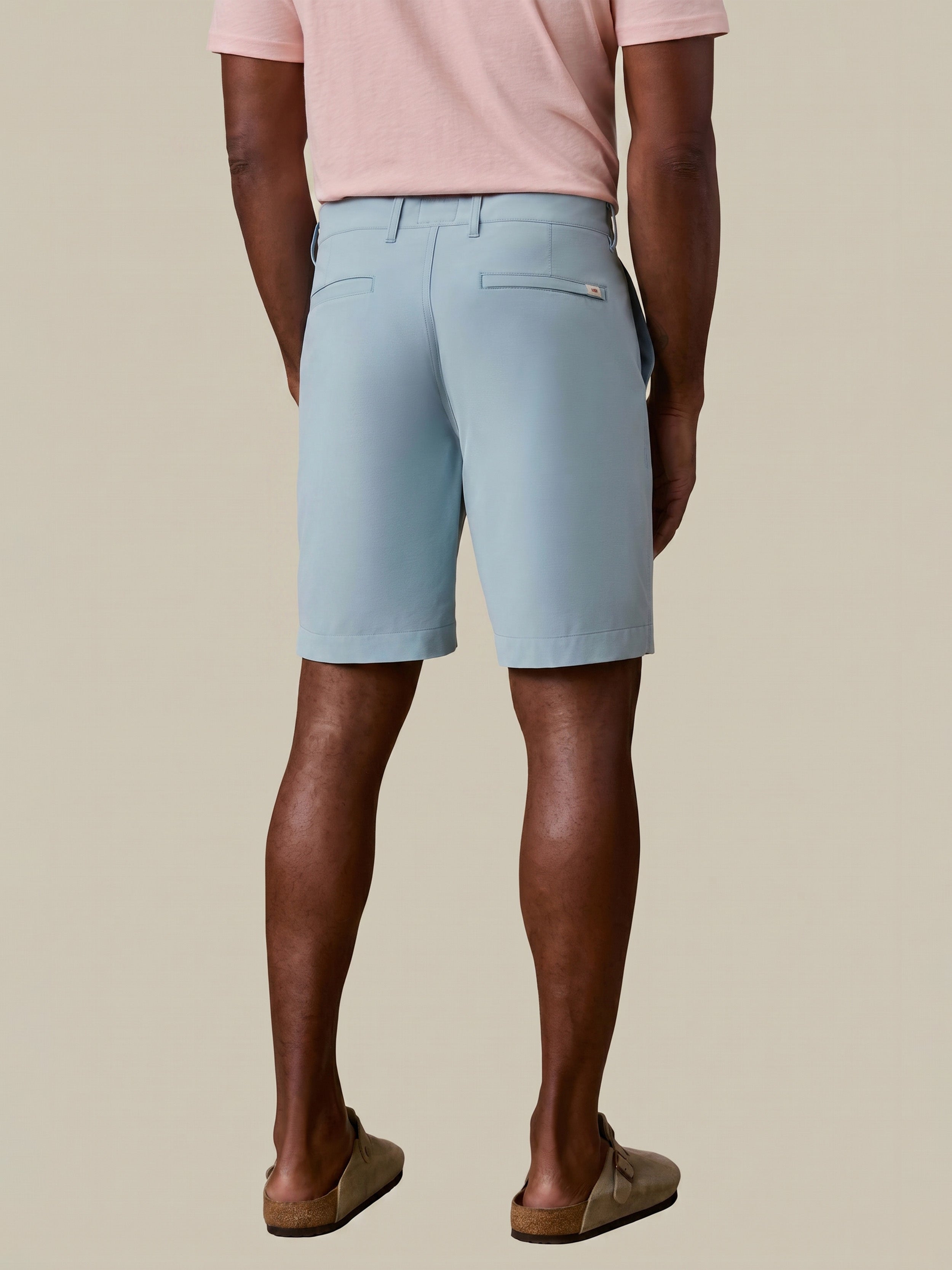 Man wearing light blue shorts and a pink shirt on a beige background