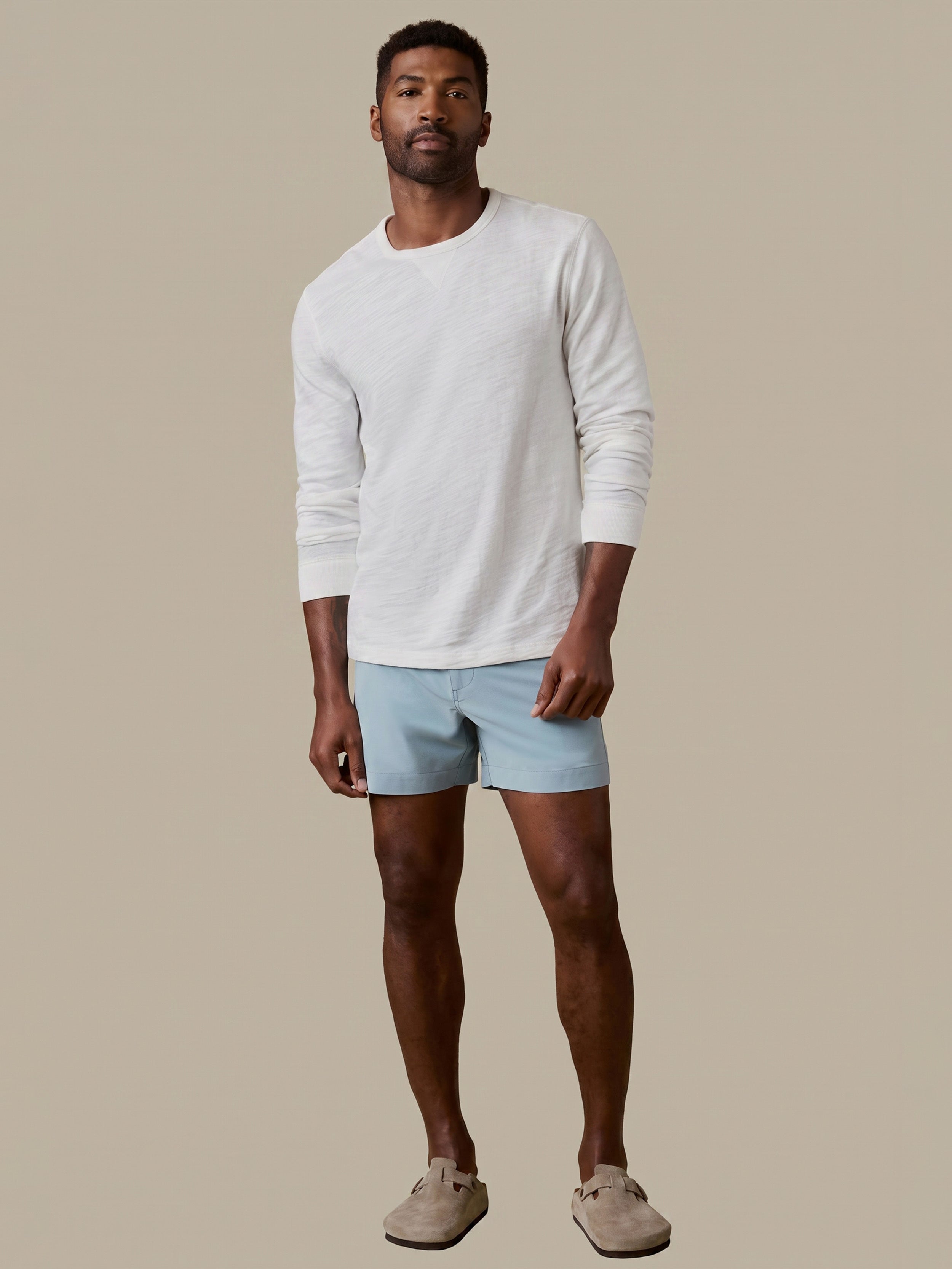 Man wearing a white long-sleeve shirt and light blue shorts against a beige background