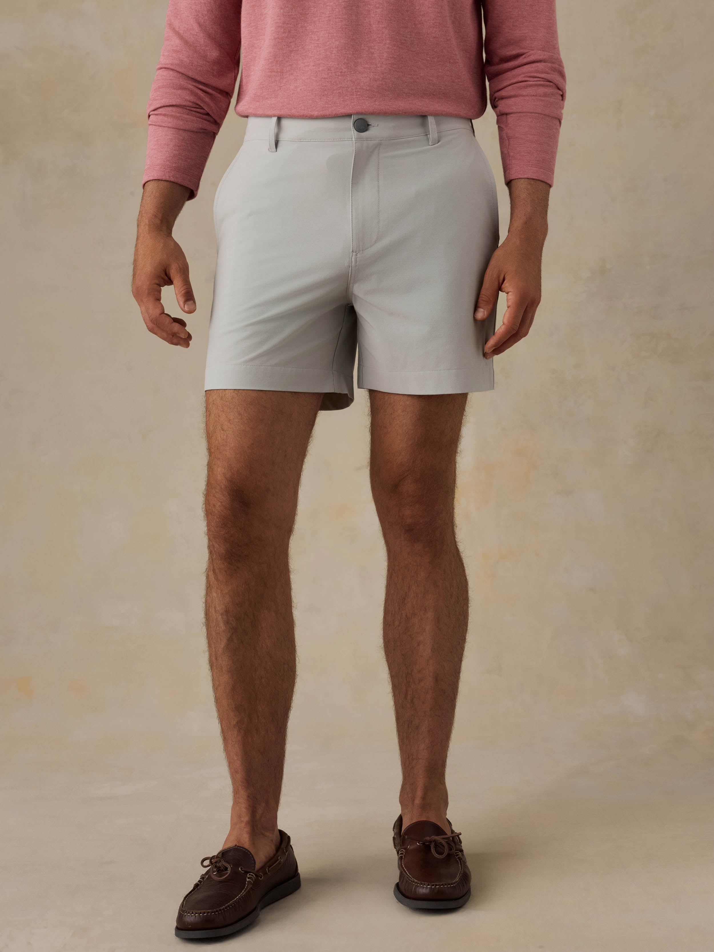 Man is wearing grey shorts and a red crewneck against a beige background