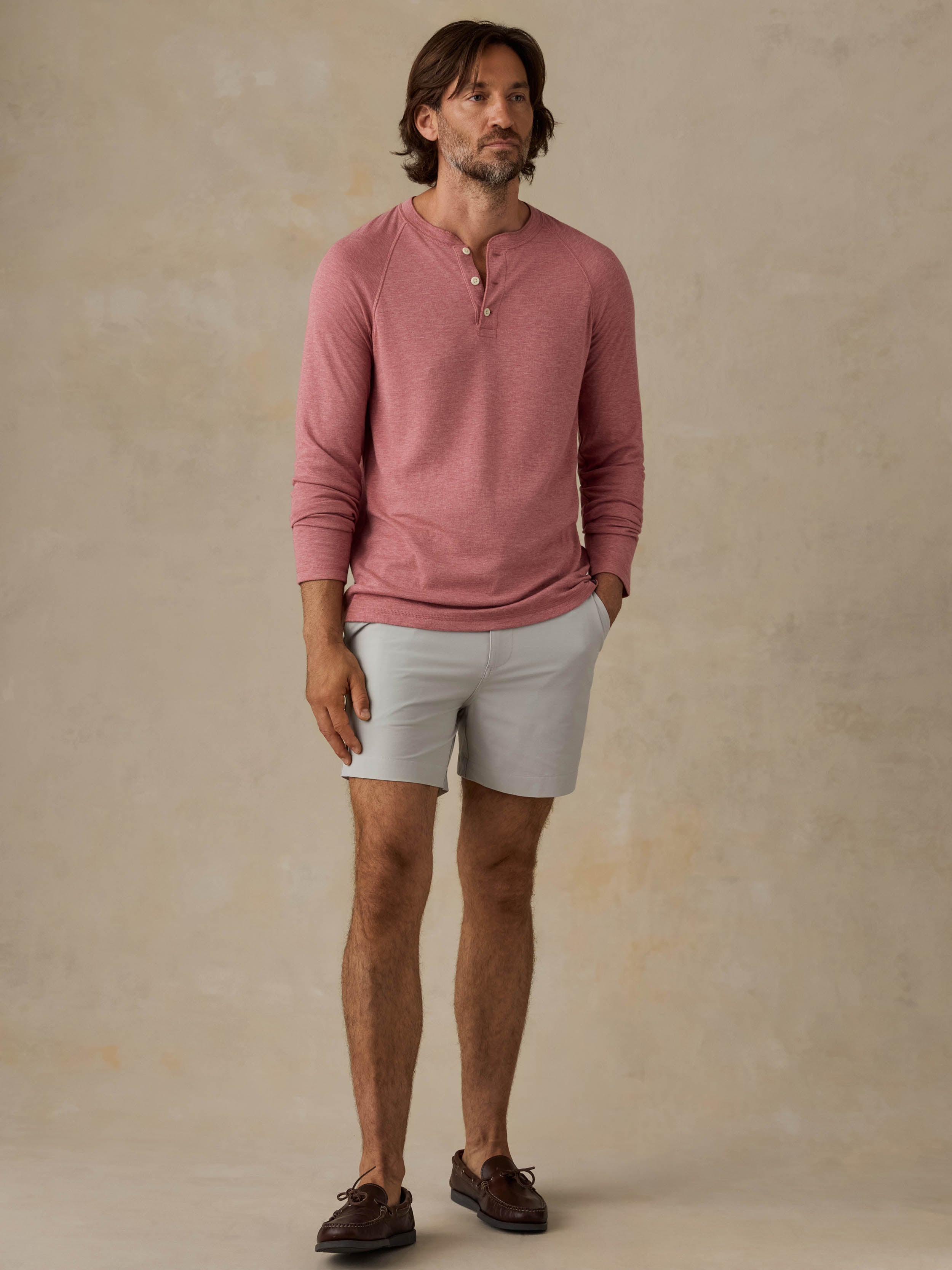 Man is wearing grey shorts and a red henley against a beige background