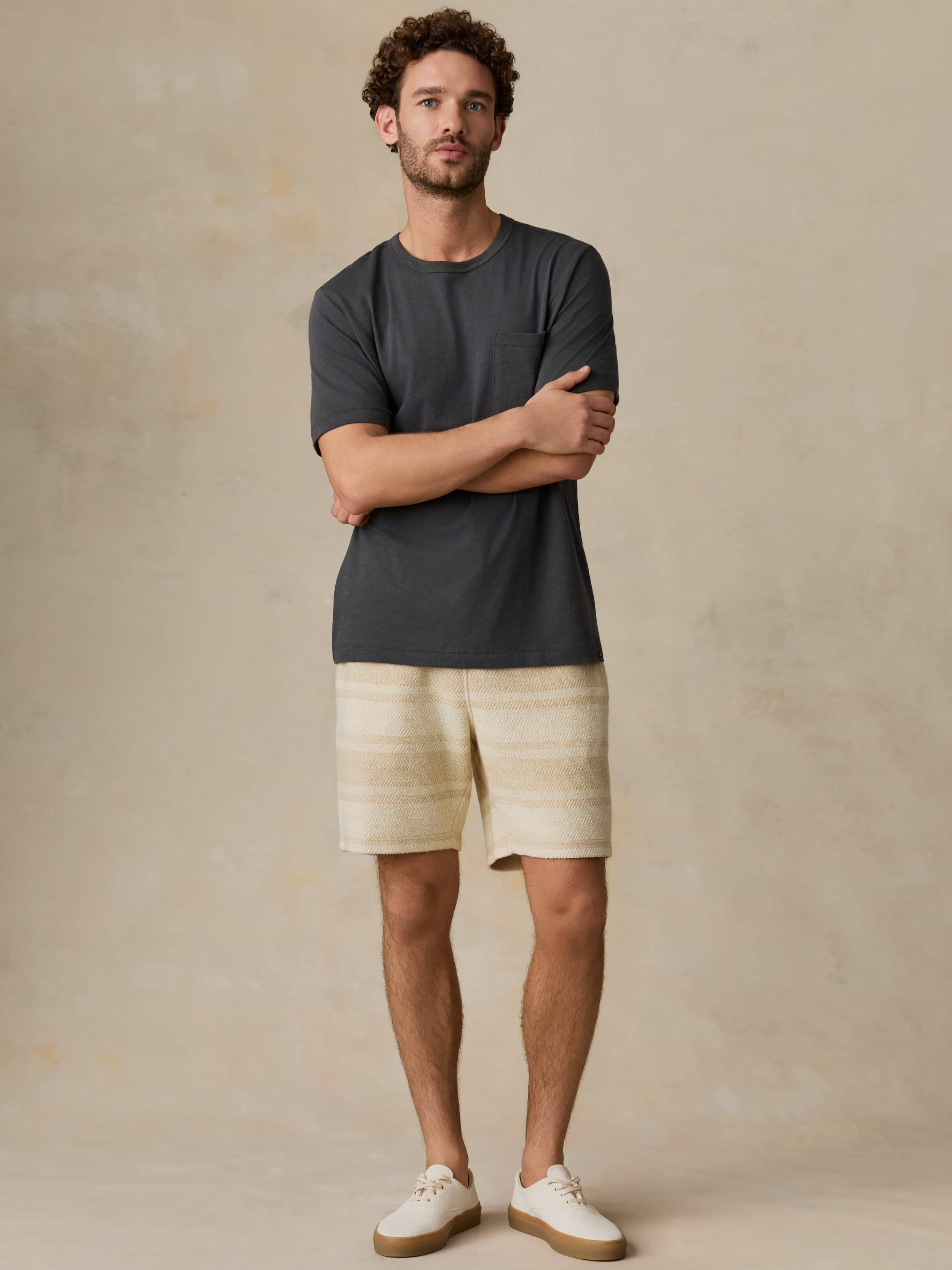 Man wearing a dark gray t-shirt and beige shorts standing against a beige background
