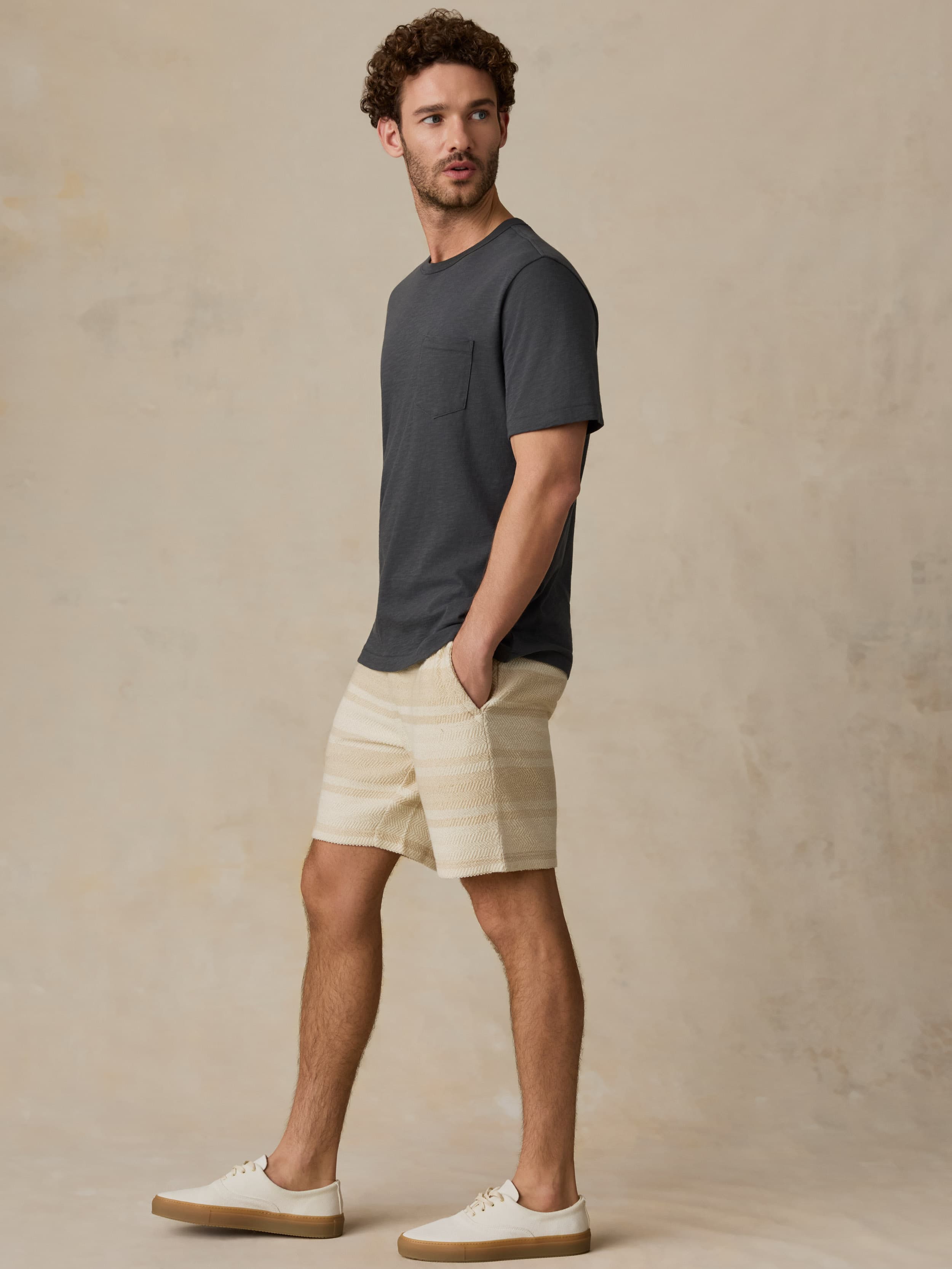Man wearing a dark gray t-shirt and beige shorts against a beige background